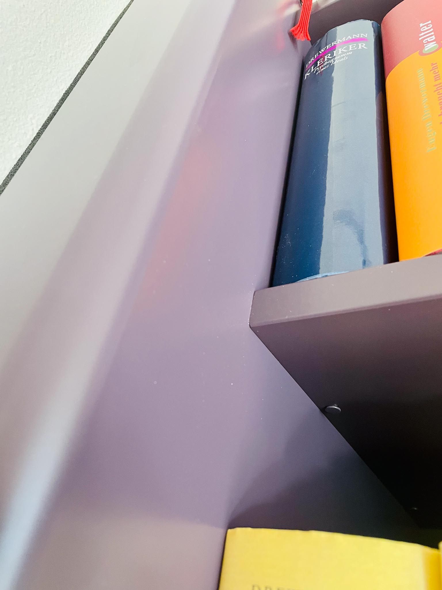 Bücher auf einem Regal; lila Regal und Wand, orange und blaue Buchumschläge.