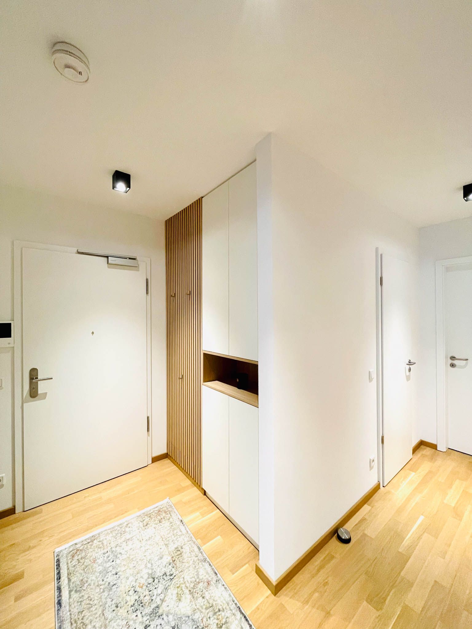 Flur mit weißen Türen, Einbauschrank, Holzböden und einem gemusterten Teppich.