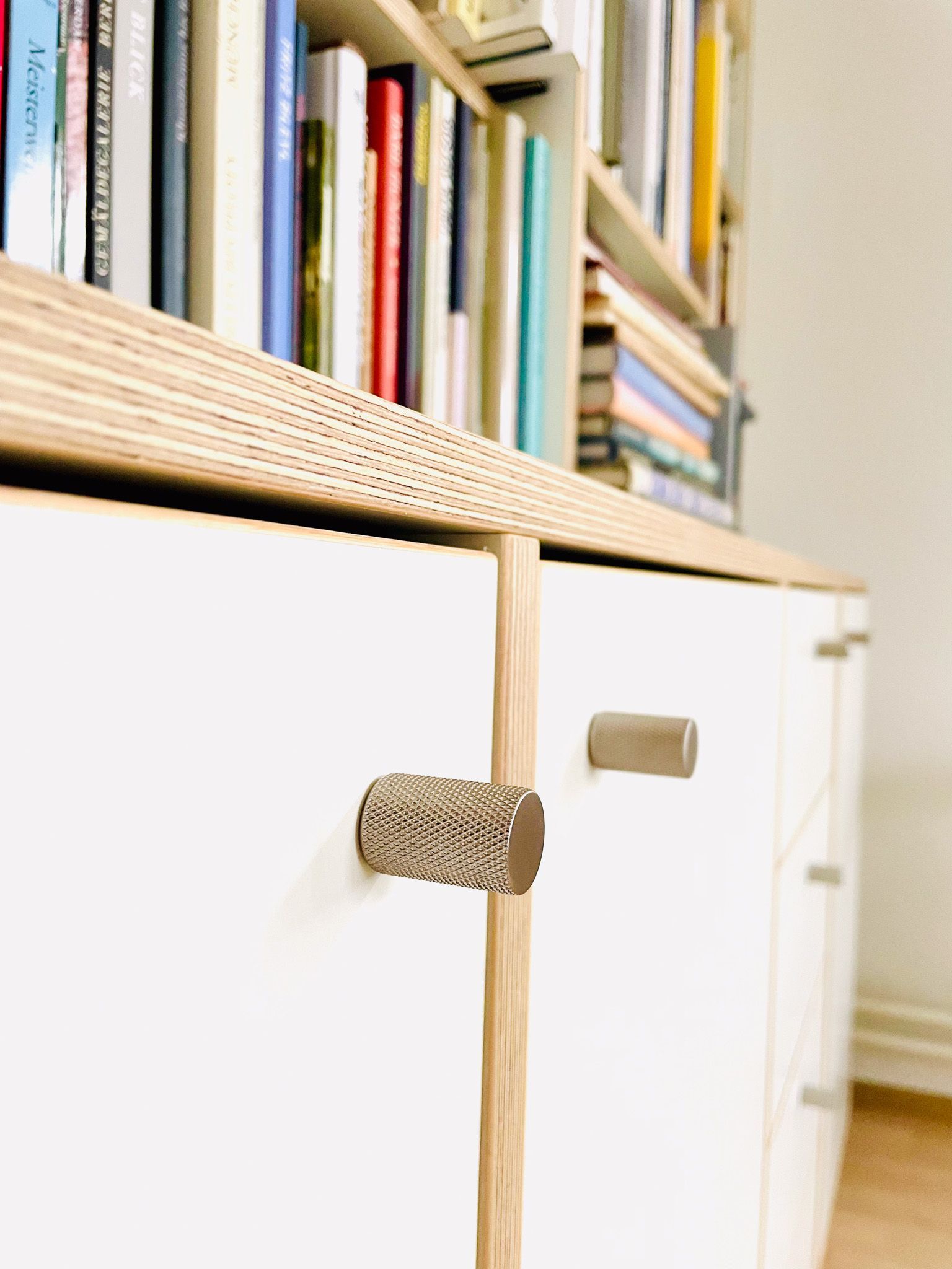 Weißer Schrank mit Holzgriffen unter einem Bücherregal.