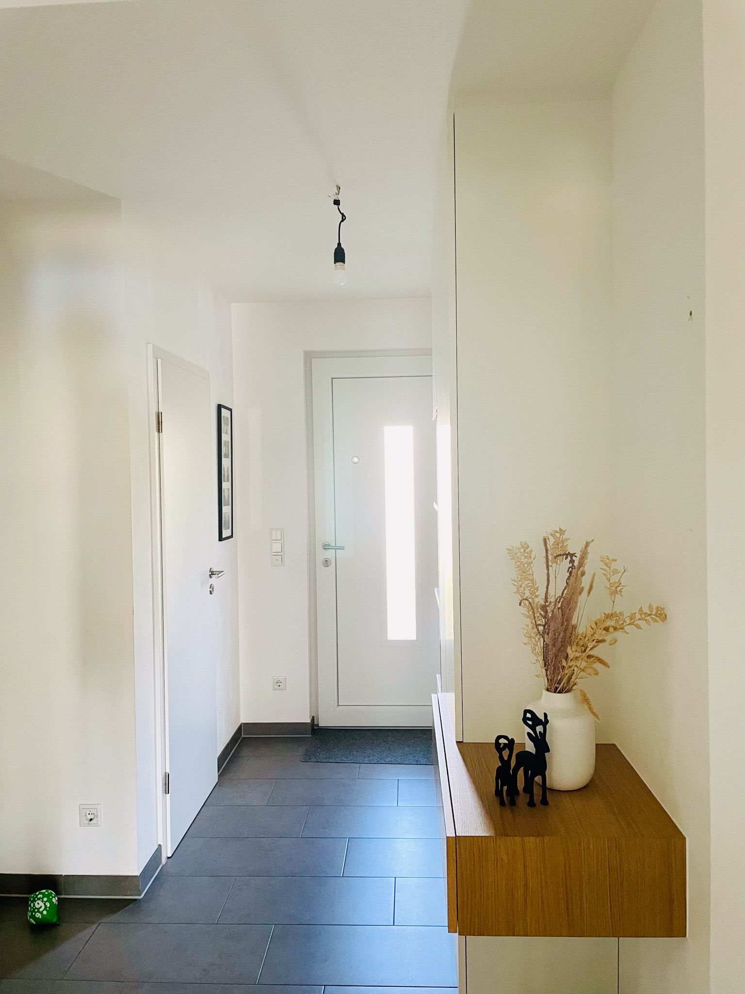 Flur mit einer weißen Tür am Ende, einem hölzernen Konsolentisch und Trockenblumen.