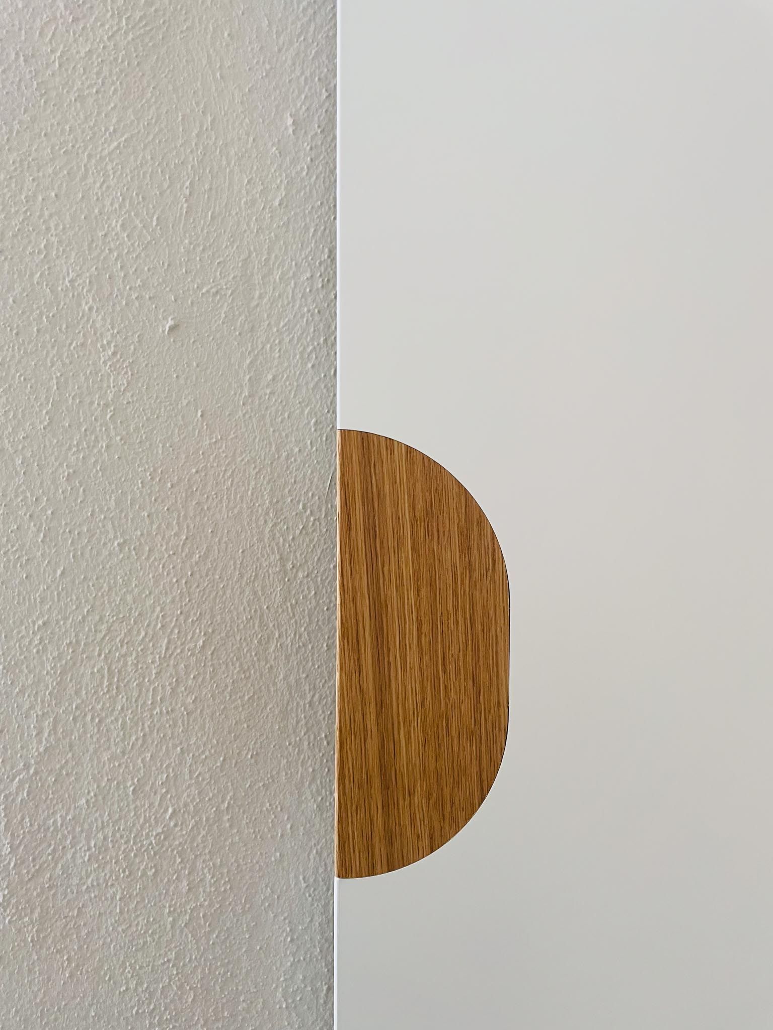 Nahaufnahme einer modernen Tür. Die eine Hälfte ist weiß, die andere Hälfte ist strukturiertes Silber, mit einem ovalen Holzgriff.