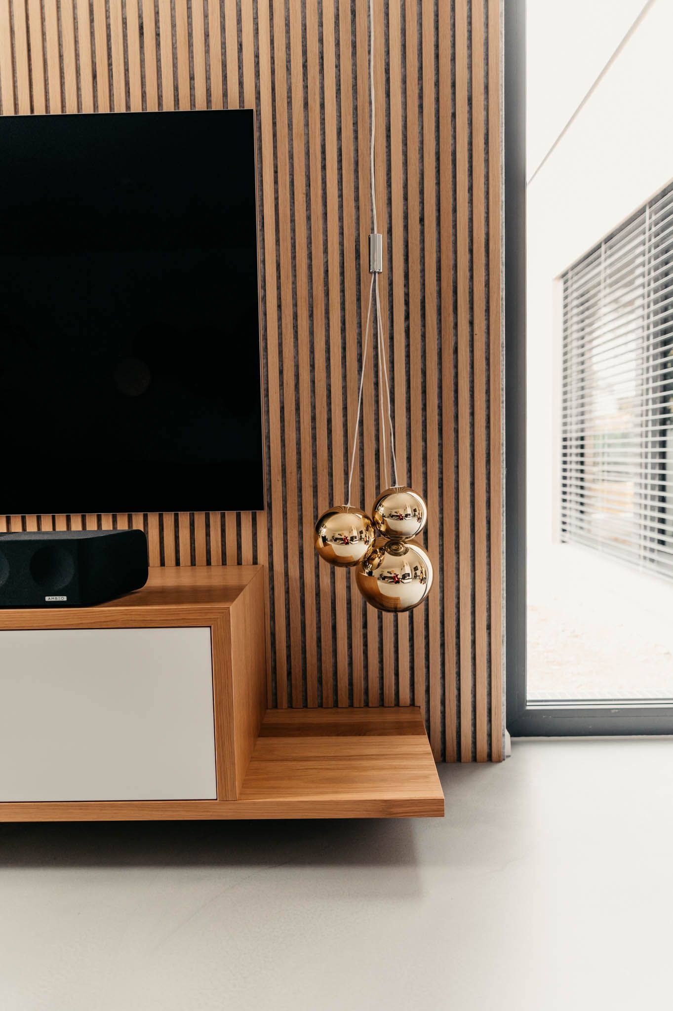 Fernseher und Soundbar auf einem Holzschrank, holzgetäfelte Wand und hängende goldene Kugeln.