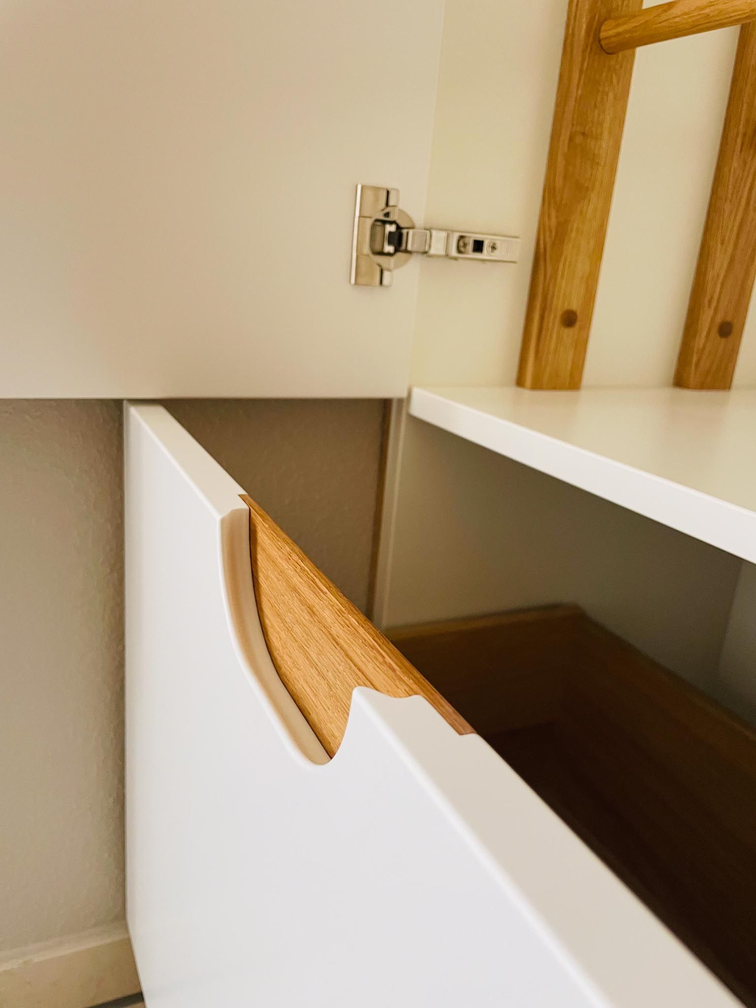 Die weiße Schranktür ist angelehnt und gibt den Blick auf ein teilweise sichtbares Holzregal und einen Behälter im Inneren frei.