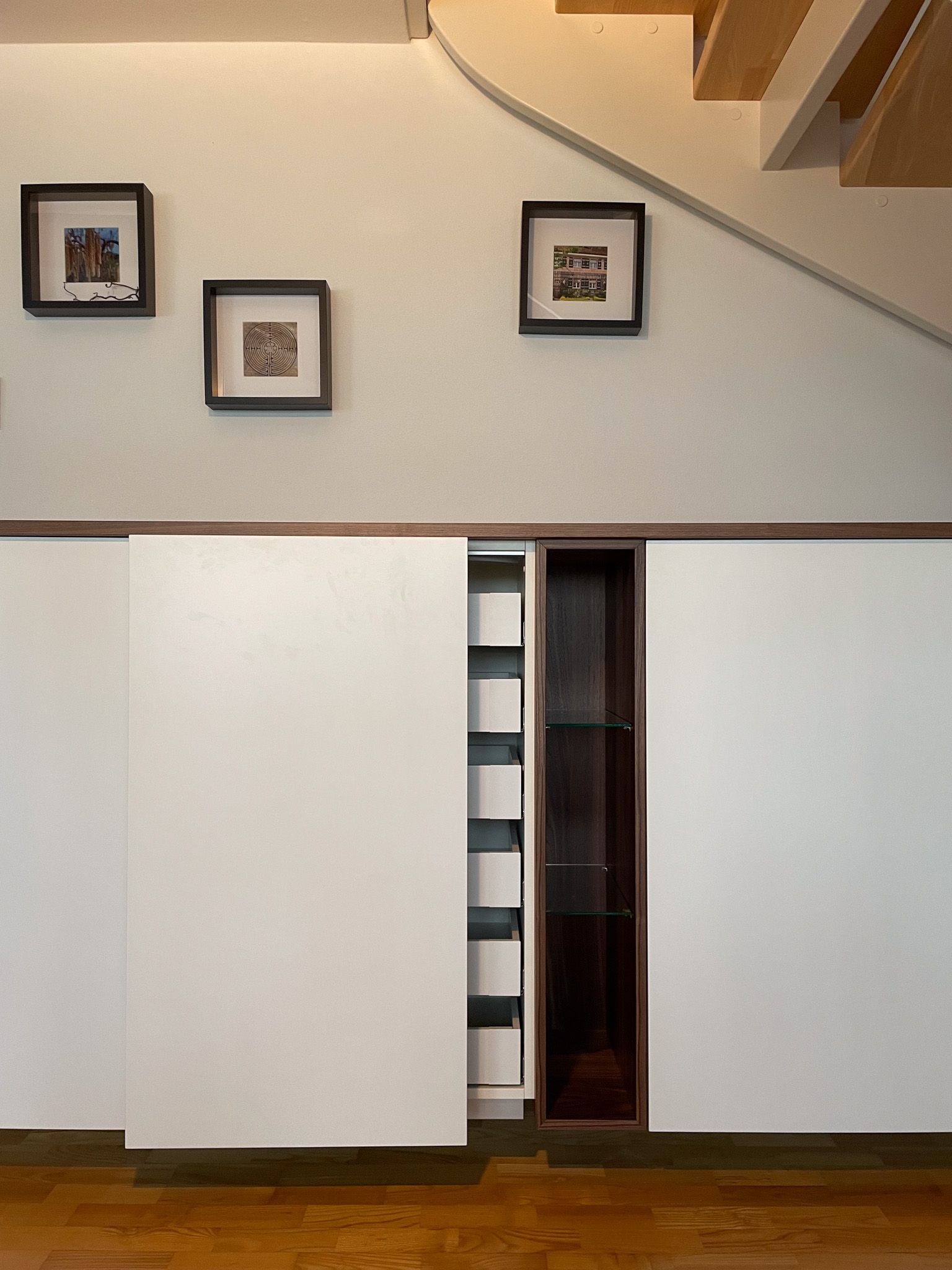 Weiße Schiebetüren für Schränke mit Kunstwerken darüber, unter einer Treppe.