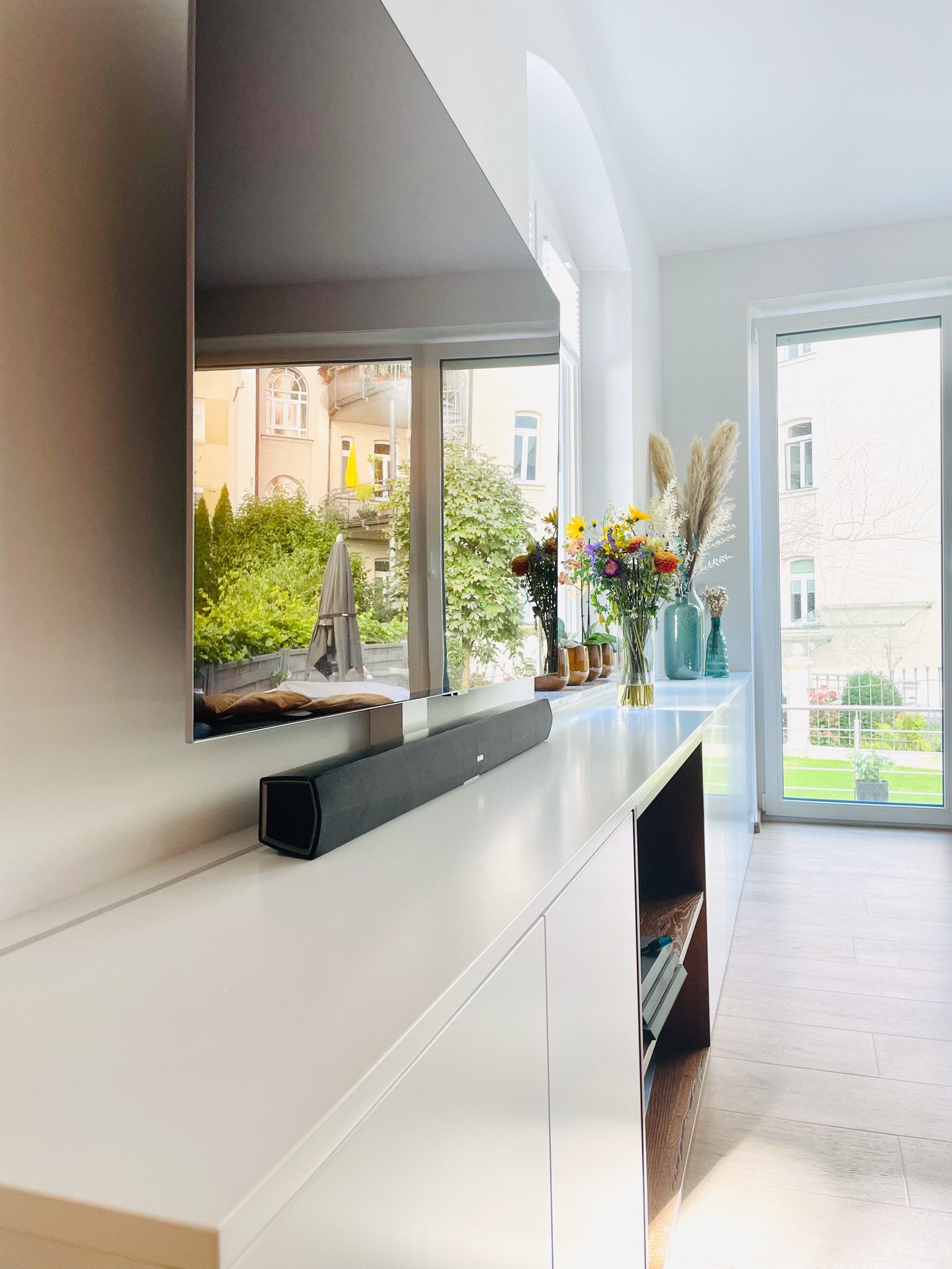 Wohnzimmer mit Fernseher, Soundbar und Blumen mit Blick auf einen Garten.
