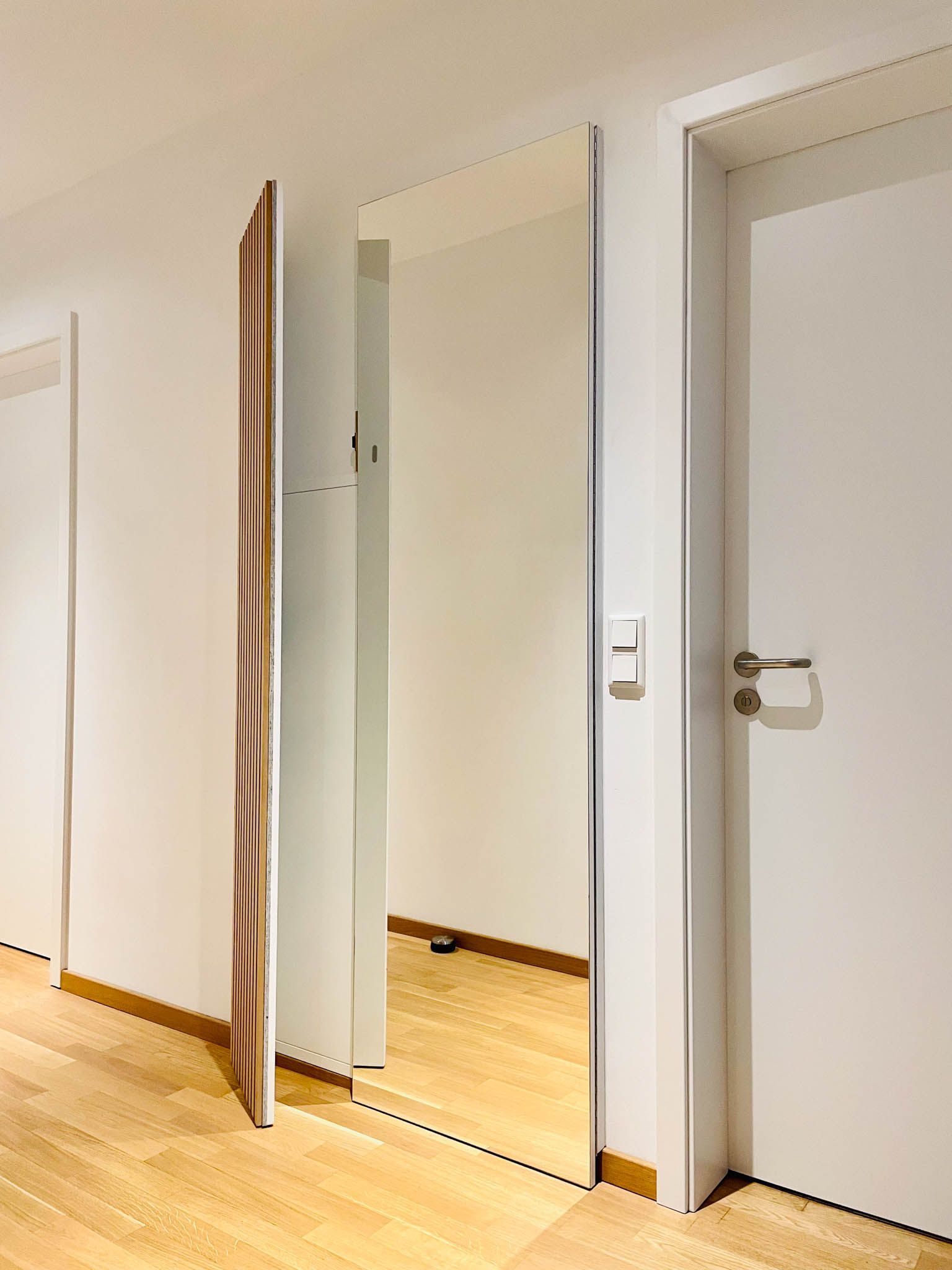 Ganzkörperspiegel im Flur mit weißen Wänden und Türen, der den Holzboden reflektiert.