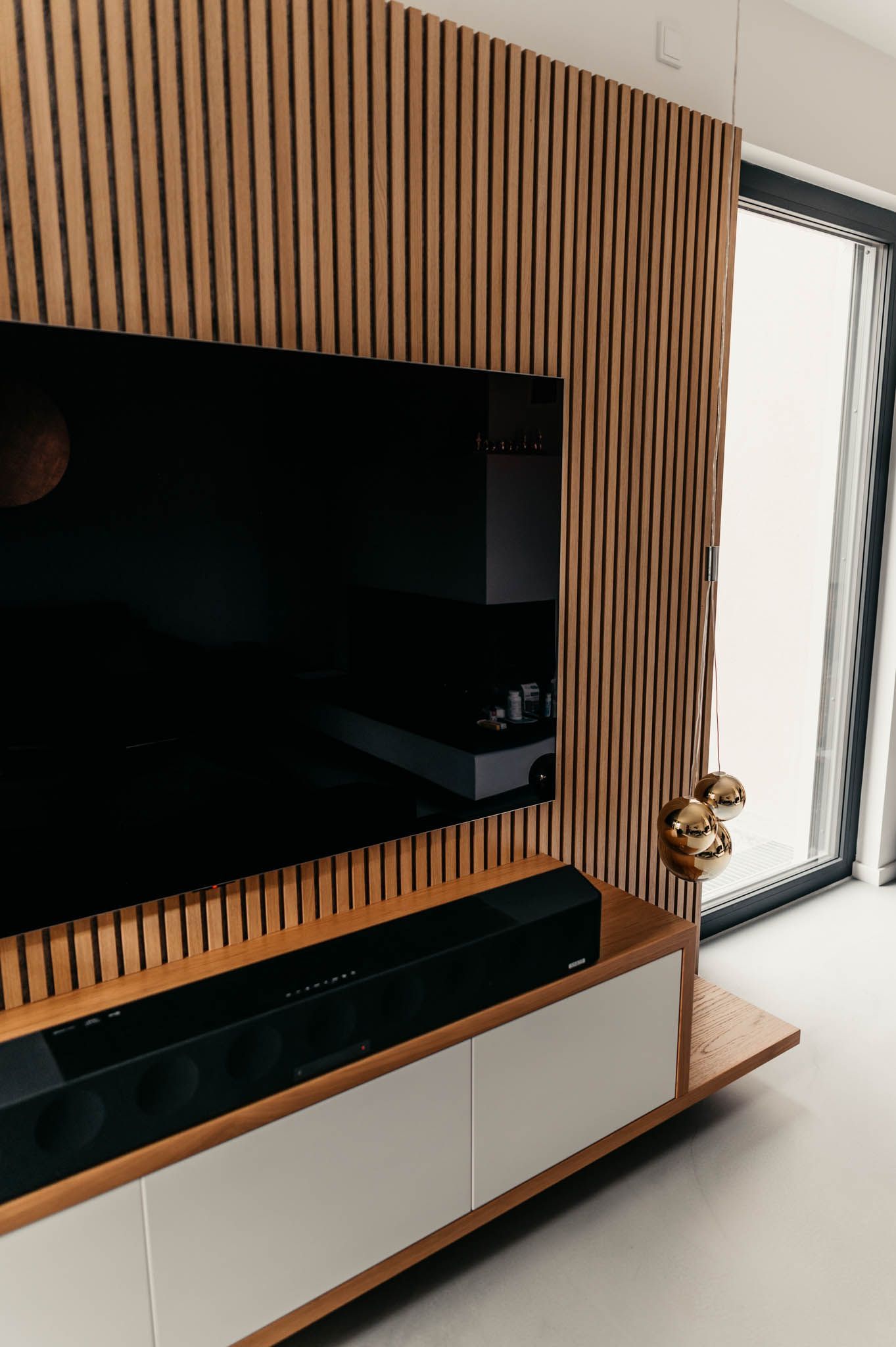 Auf einer Holzplatte montierter Fernseher, Soundbar und ein weißer Schrank. Golddekor in einem modernen Wohnraum.
