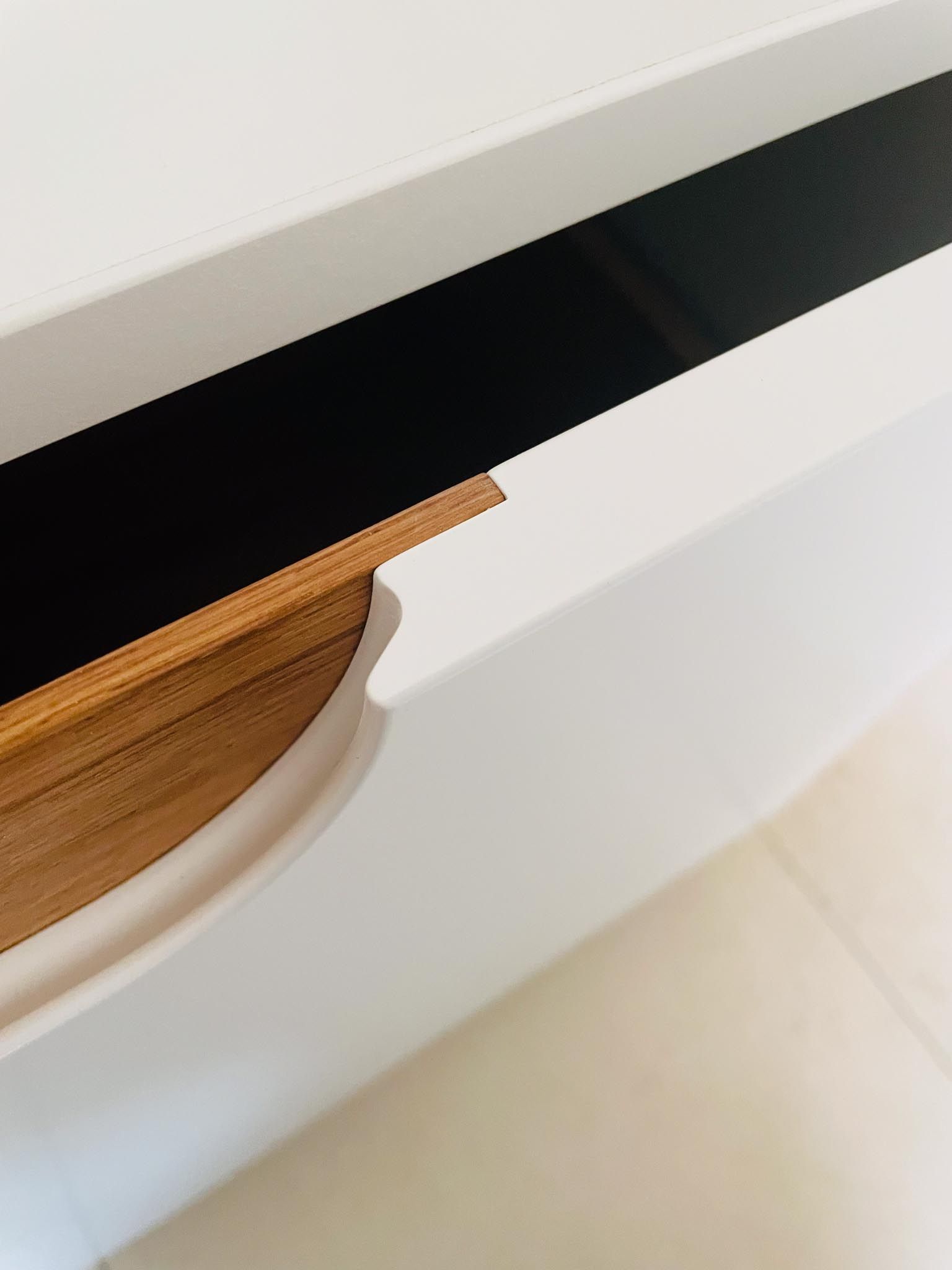Weißer Schrank mit schwarzem Streifen und Schubladengriff aus Holz.