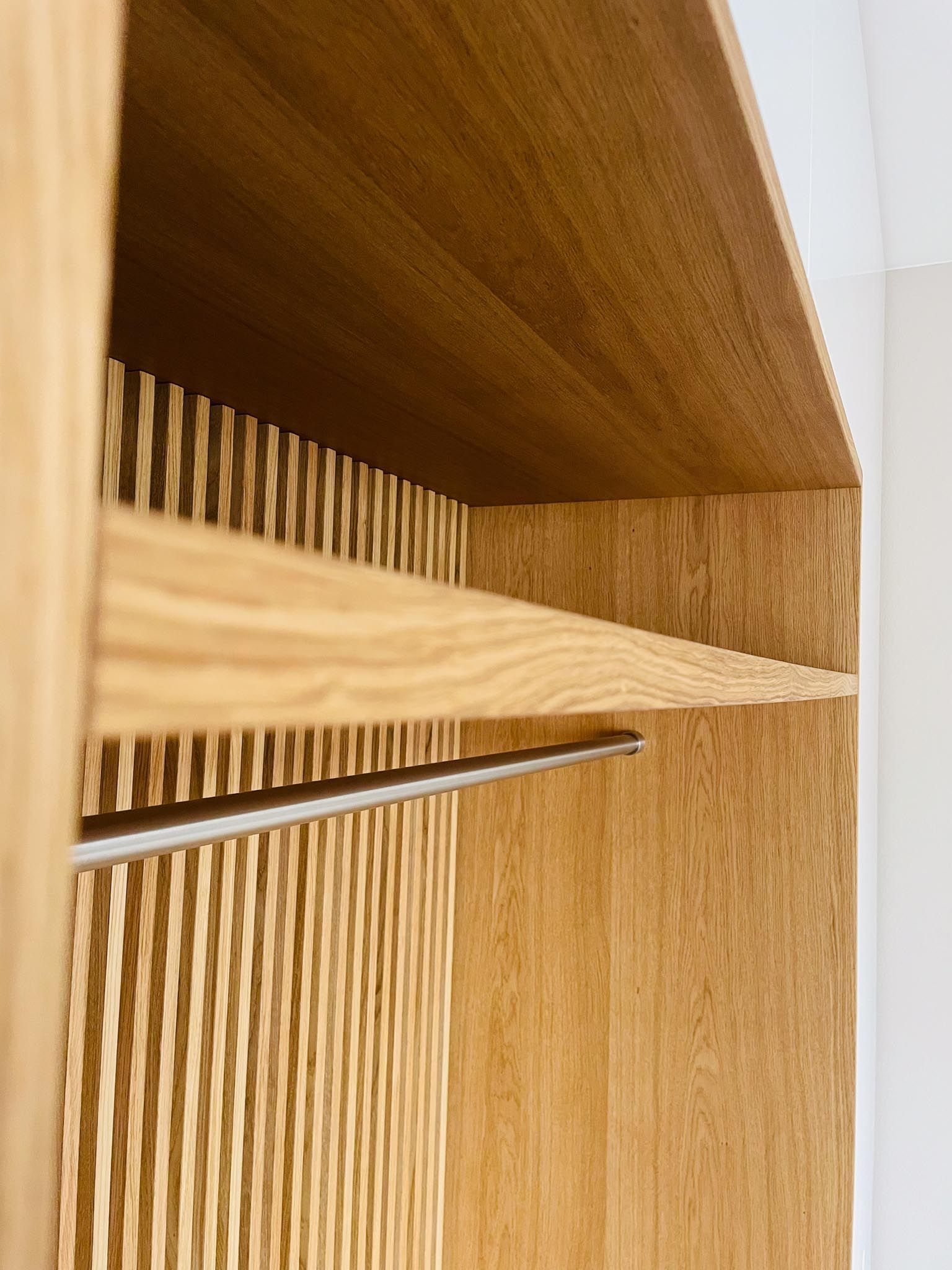 Schrankinnenraum aus Holz mit Einlegeböden, Kleiderstange und gerippter Seitenwand.