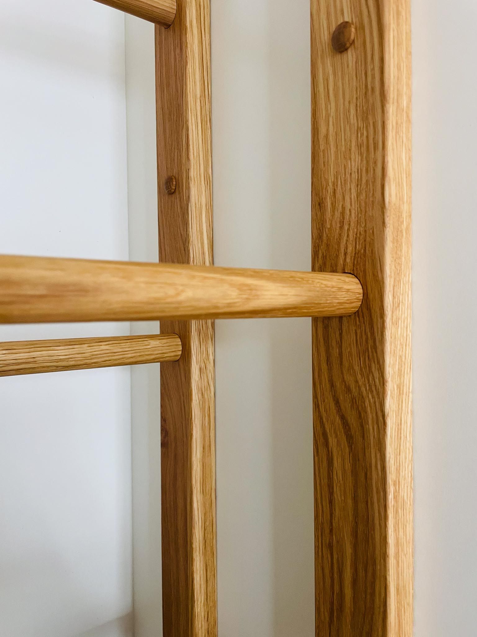 Leiterartige Holzkonstruktion vor einer weißen Wand. Horizontale Sprossen und vertikale Stützen, alles in natürlichen Holztönen.