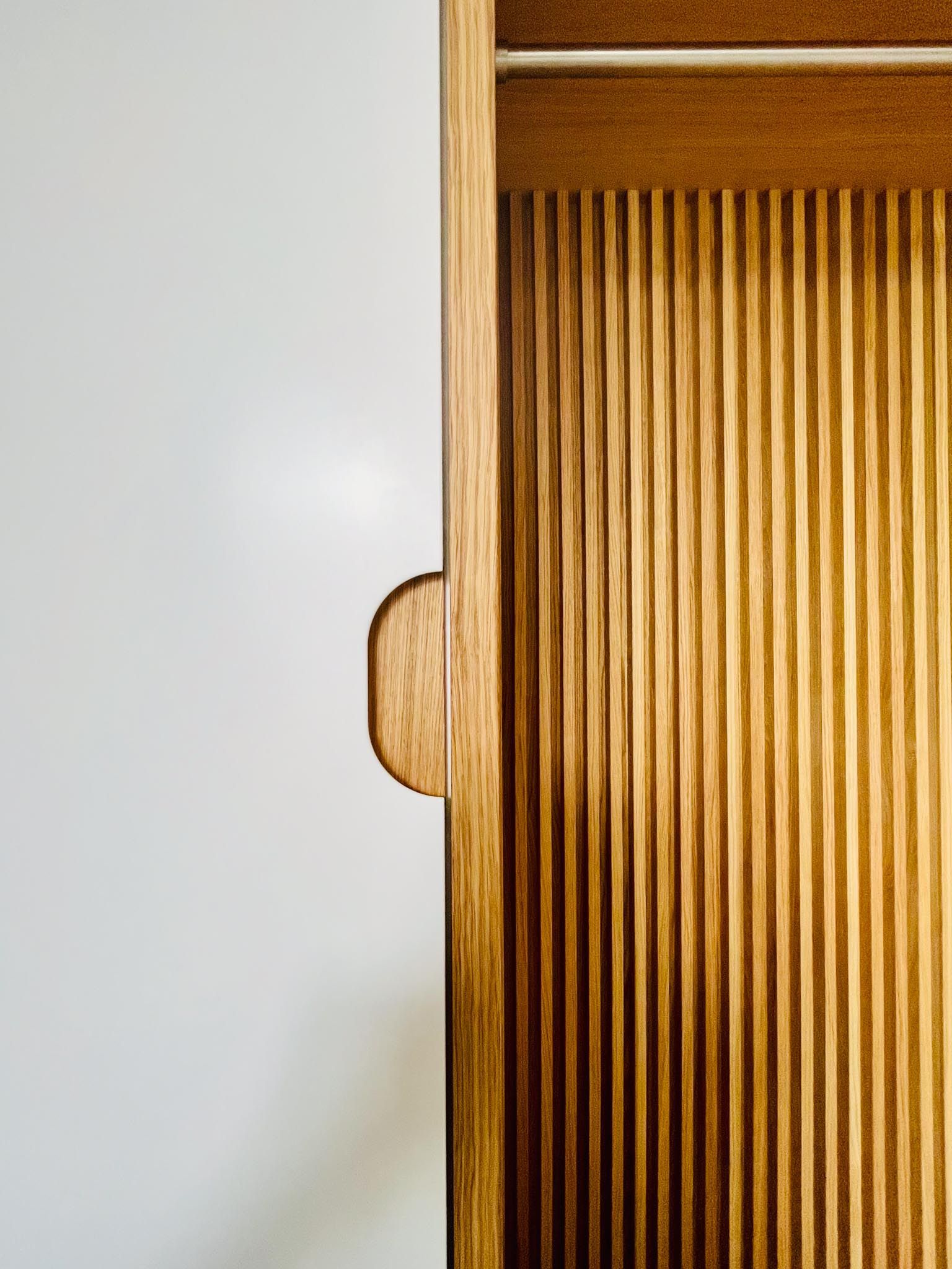 Holztür mit vertikalen Rillen, Griff und weißer Wand.