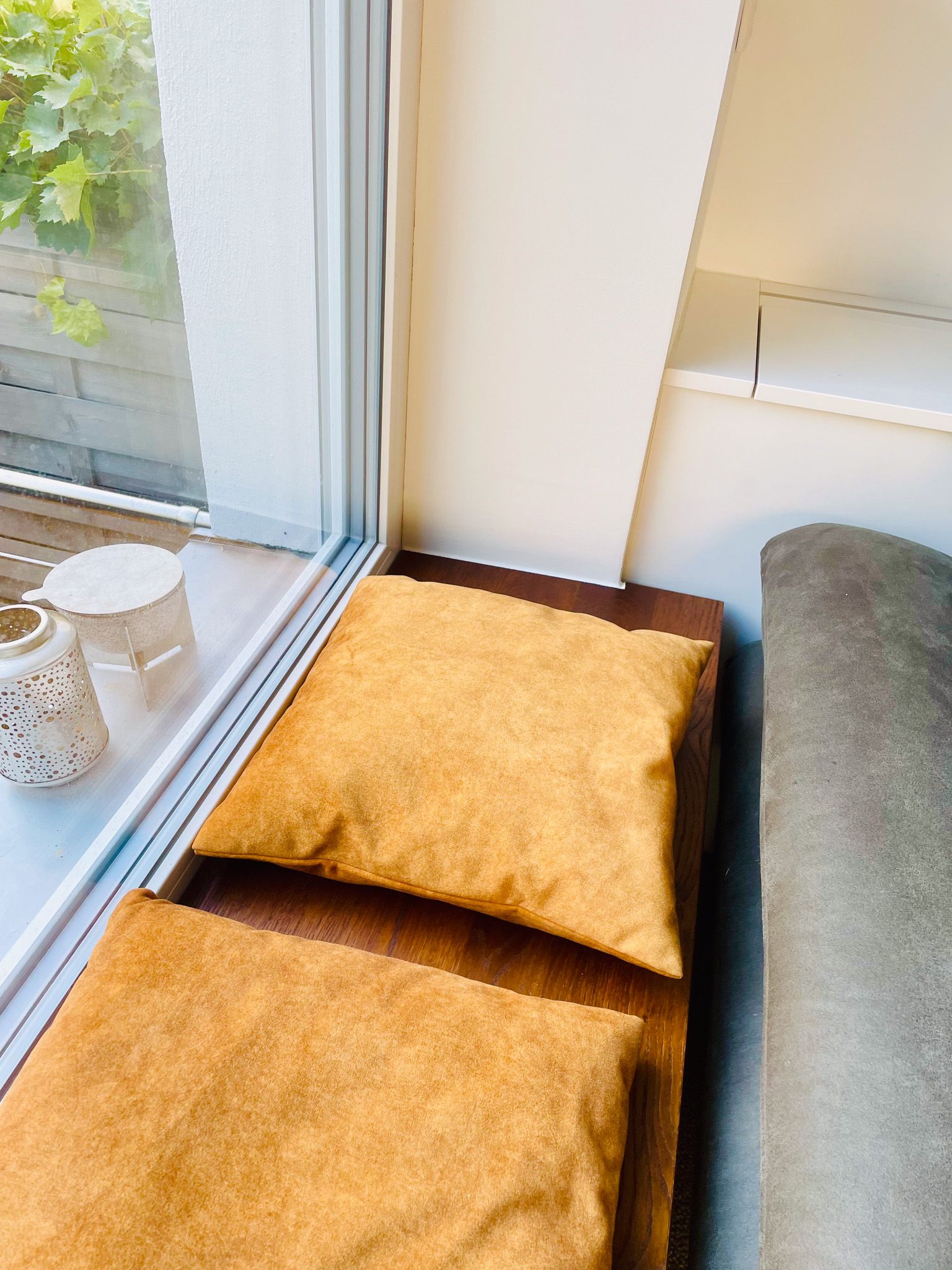 Zwei goldene Kissen auf einem hölzernen Fenstersitz, in der Nähe eines Fensters mit Aussicht.