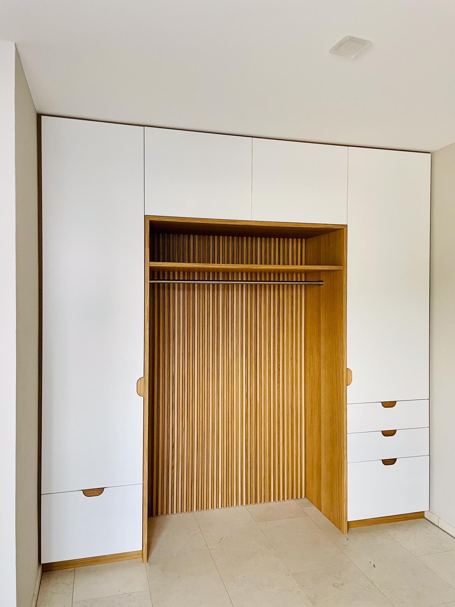 Weißer und hölzerner Kleiderschrank mit Schubladen, Kleiderstange und vertikaler Holzvertäfelung.