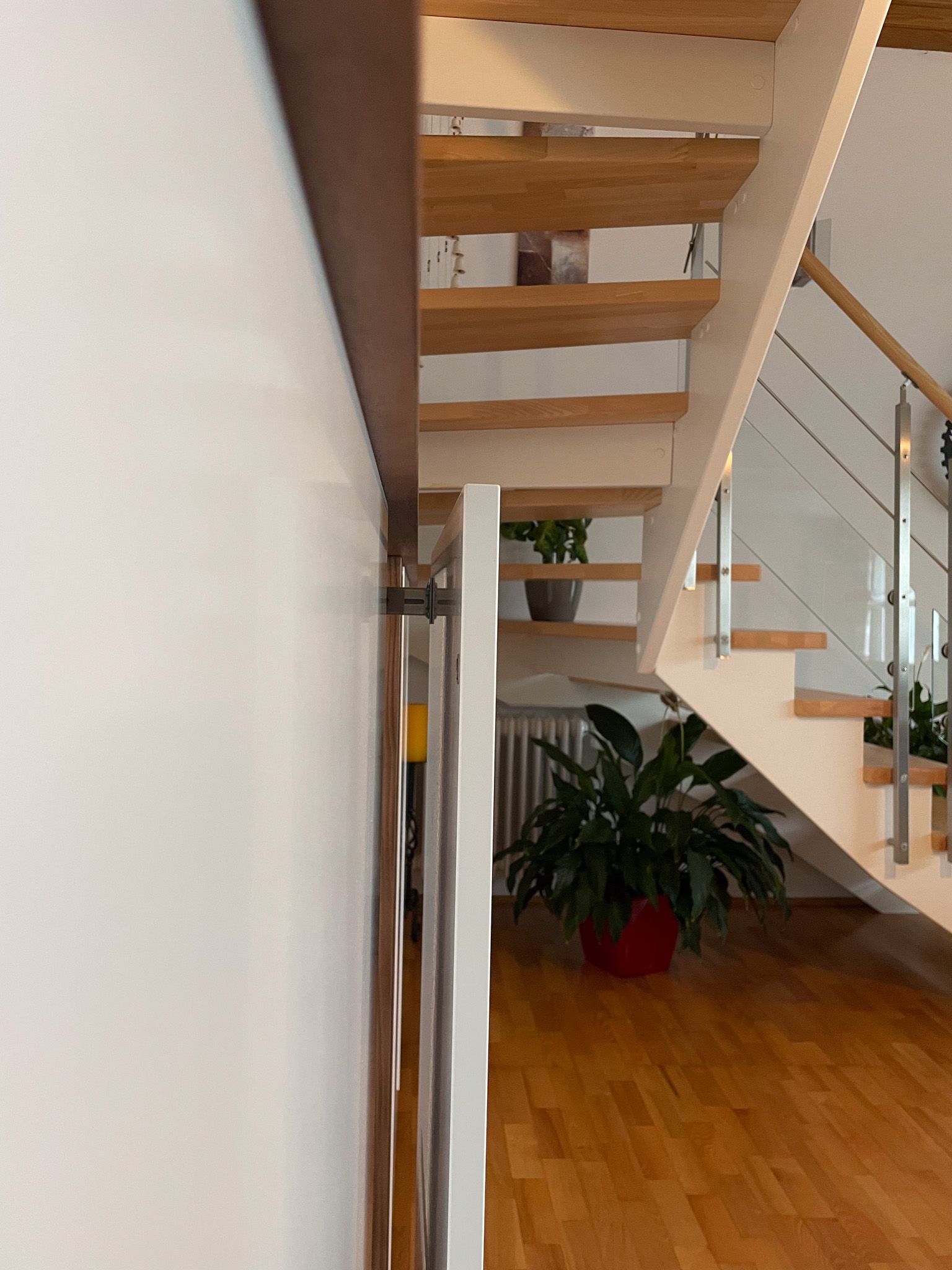 Treppe mit Holzstufen und Glasgeländer. Auf dem Boden steht eine Pflanze in einem roten Topf.