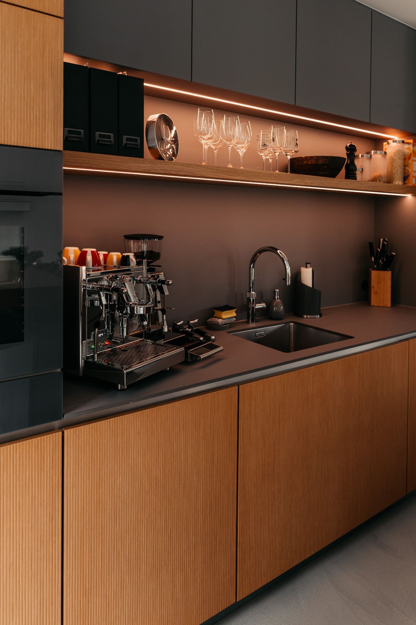 Moderne Küche mit Holzschränken, Espressomaschine, Spüle und Regalen mit Glaswaren.