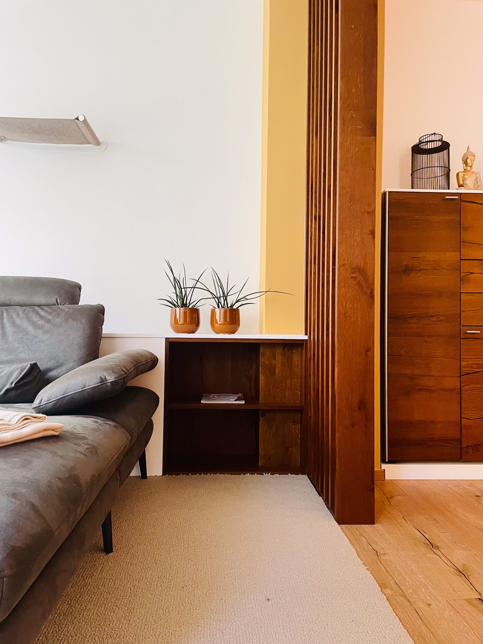 Graues Sofa, Holztrennwand mit Regal und dunkler Holzschrank in einem Wohnzimmer.