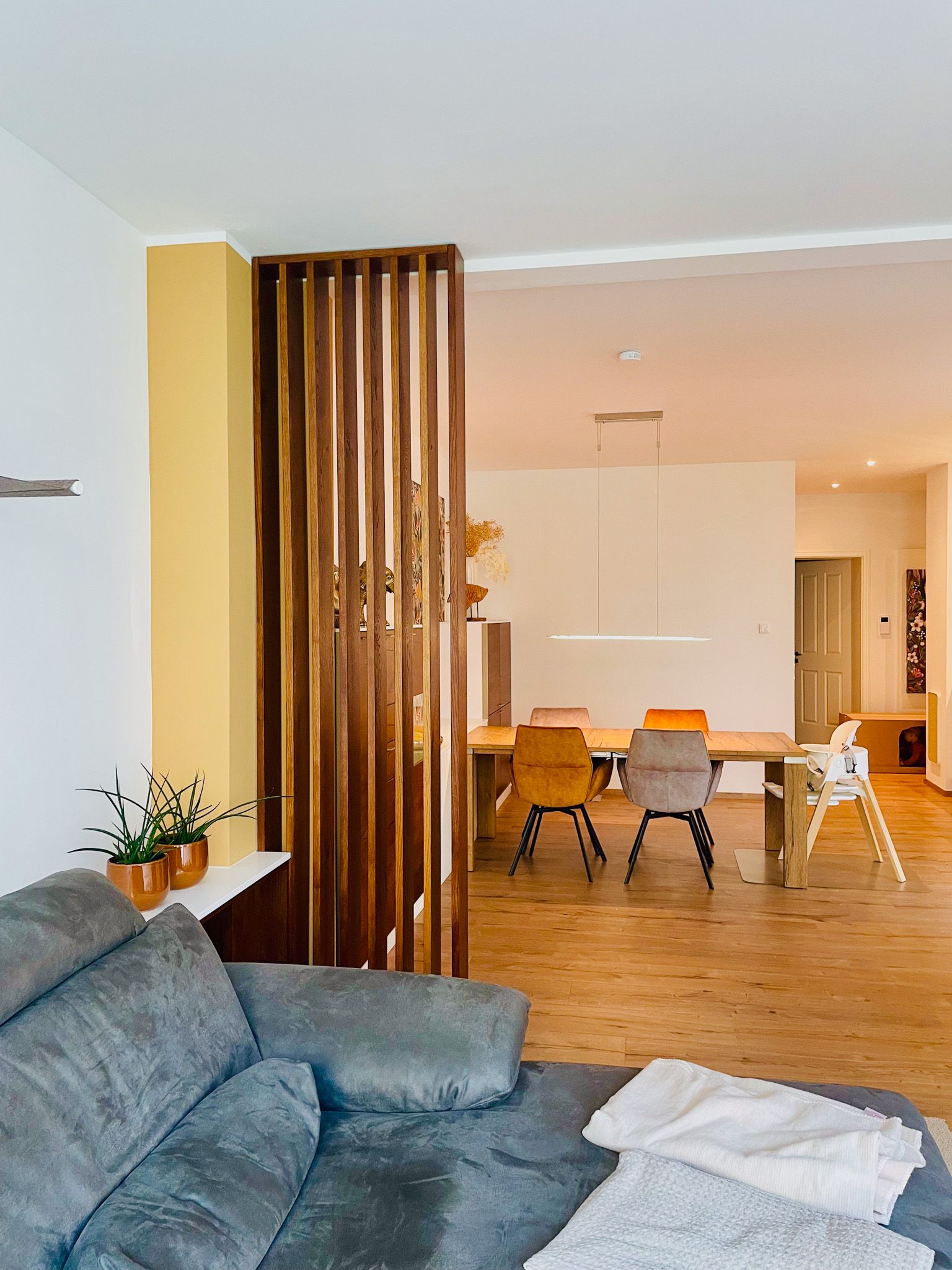 Wohnzimmer mit einem hölzernen Raumteiler, der zu einem Essbereich mit Tisch und Stühlen führt.