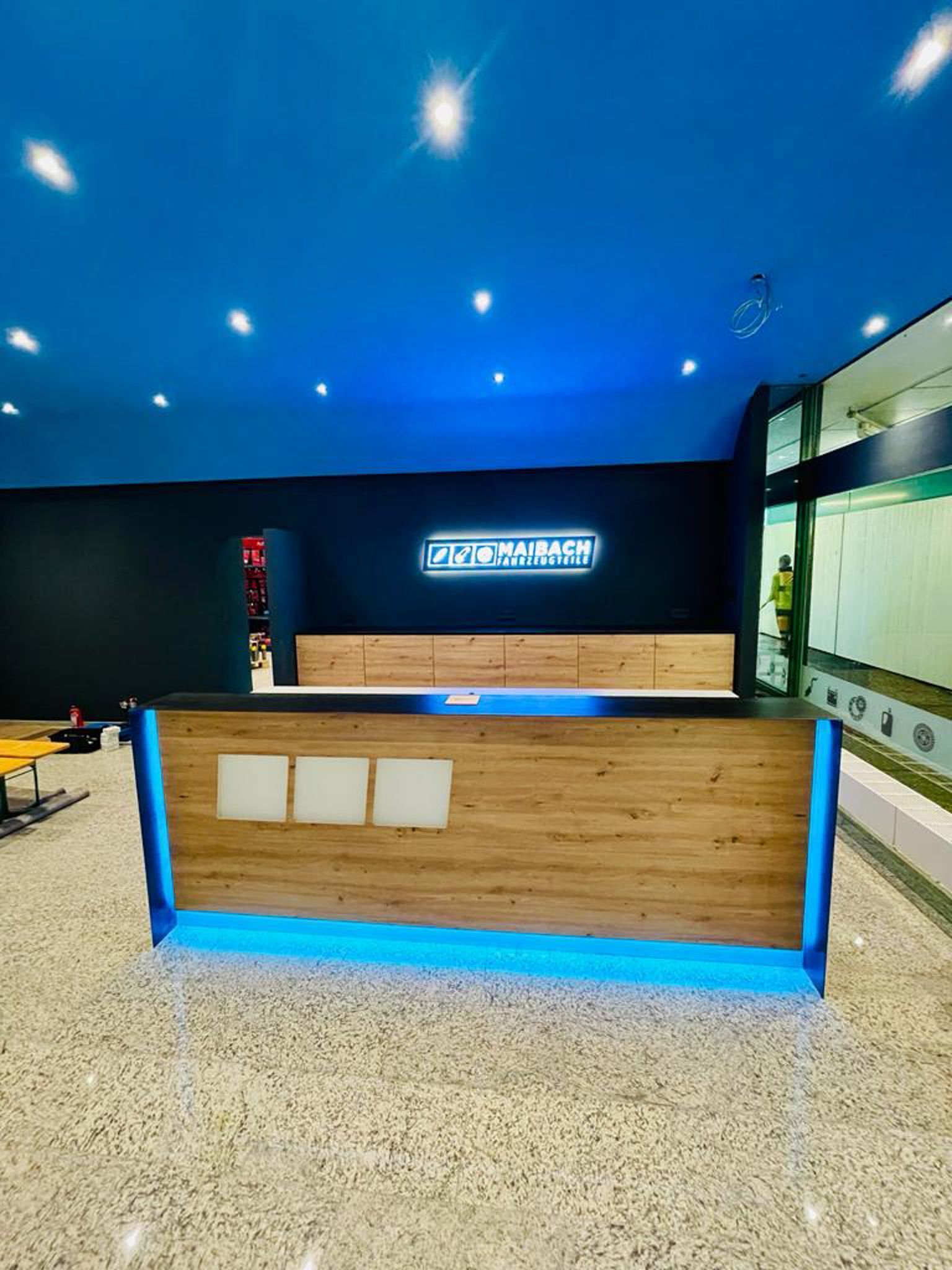 Rezeptionstresen mit Holzfront, blauer Beleuchtung und einem Schild mit der Aufschrift „Tastation“ an einer blauen Decke.