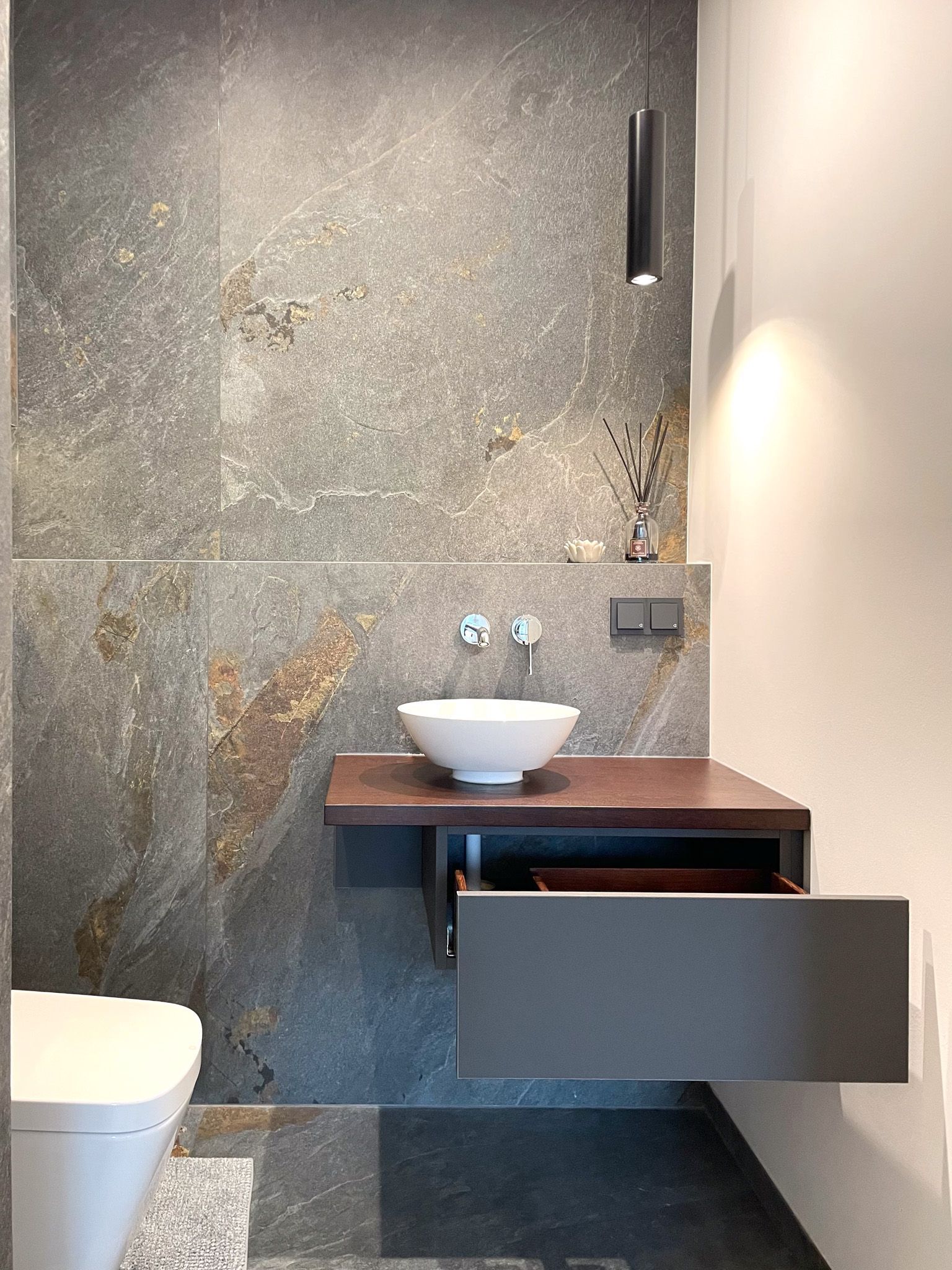 Modernes Badezimmer mit schwebendem Waschbecken und Schublade, Akzentwand aus Stein und Toilette.