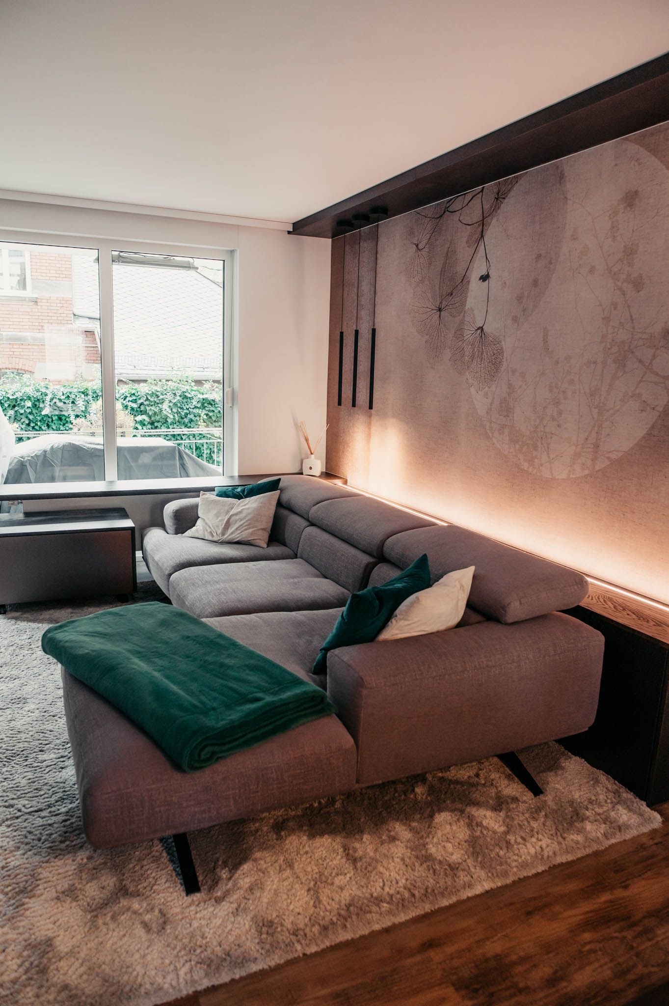 Graues Sofagarnitur mit grünen und weißen Kissen und Decken in einem modernen Wohnzimmer.