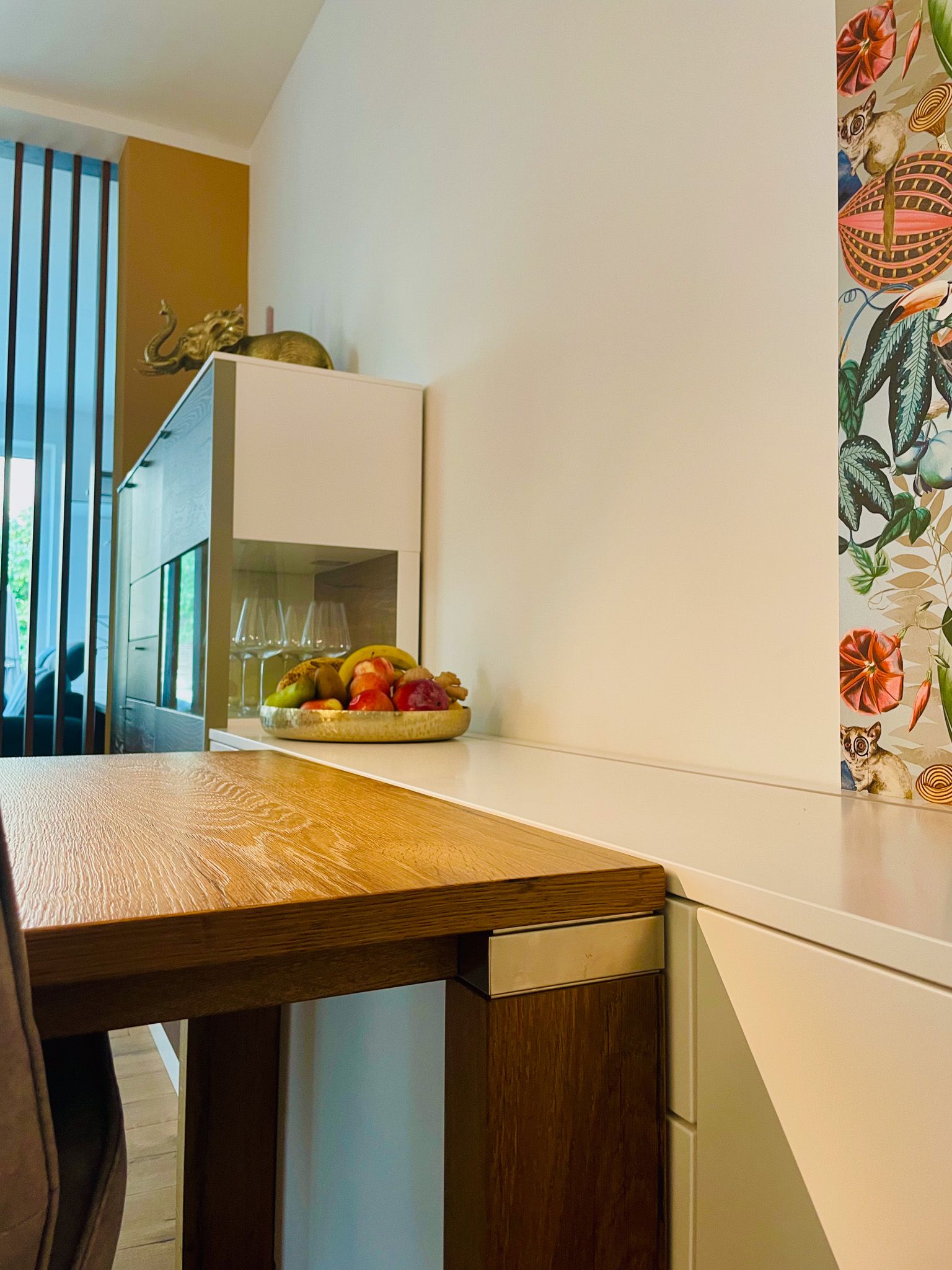 Küchentheke mit Holztisch, Obst und weißen Schränken. Bunter Vorhang auf der rechten Seite.