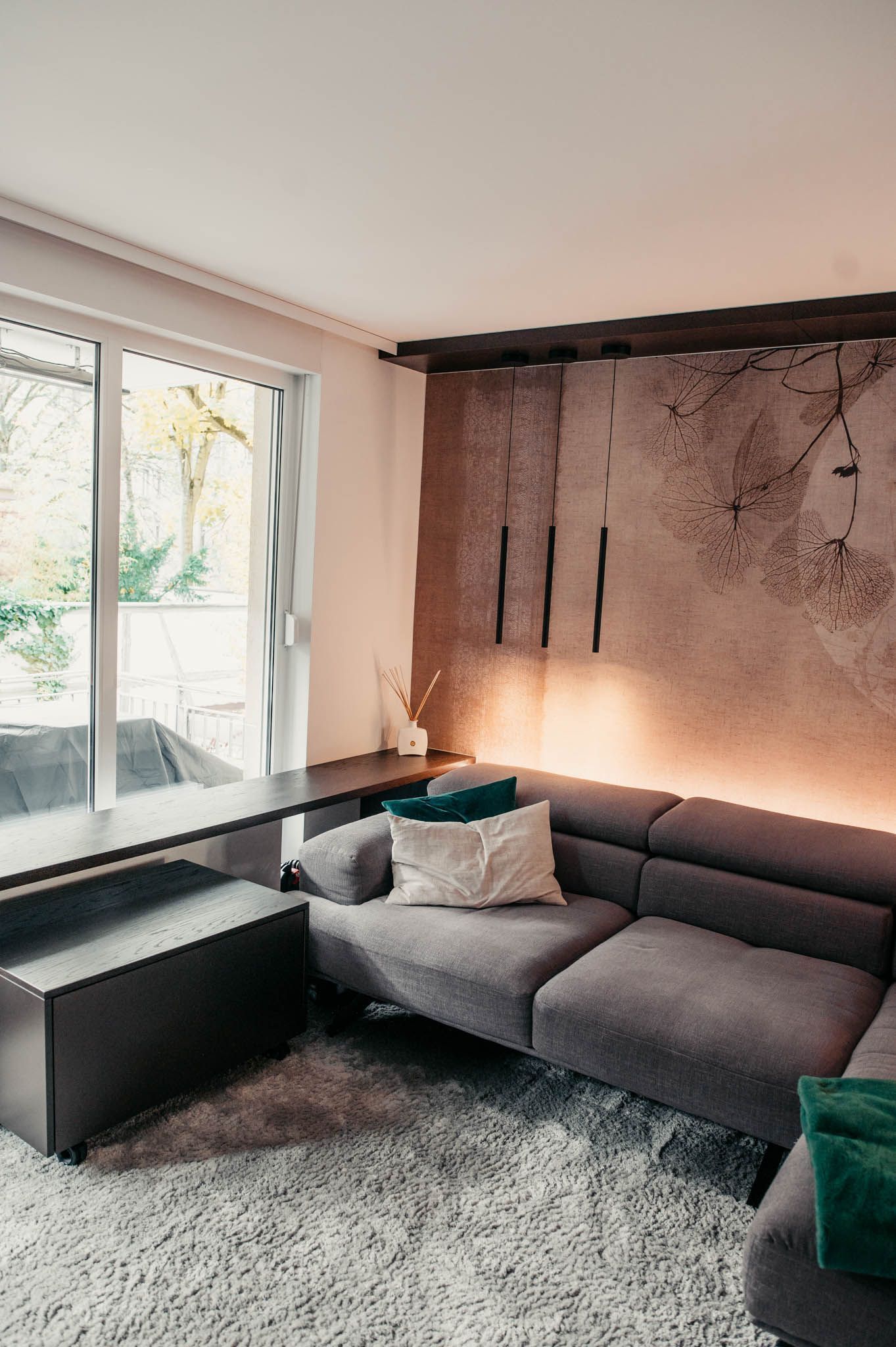 Graues Sofagarnitur in einem modernen Wohnzimmer mit großem Fenster und strukturierter Wand.