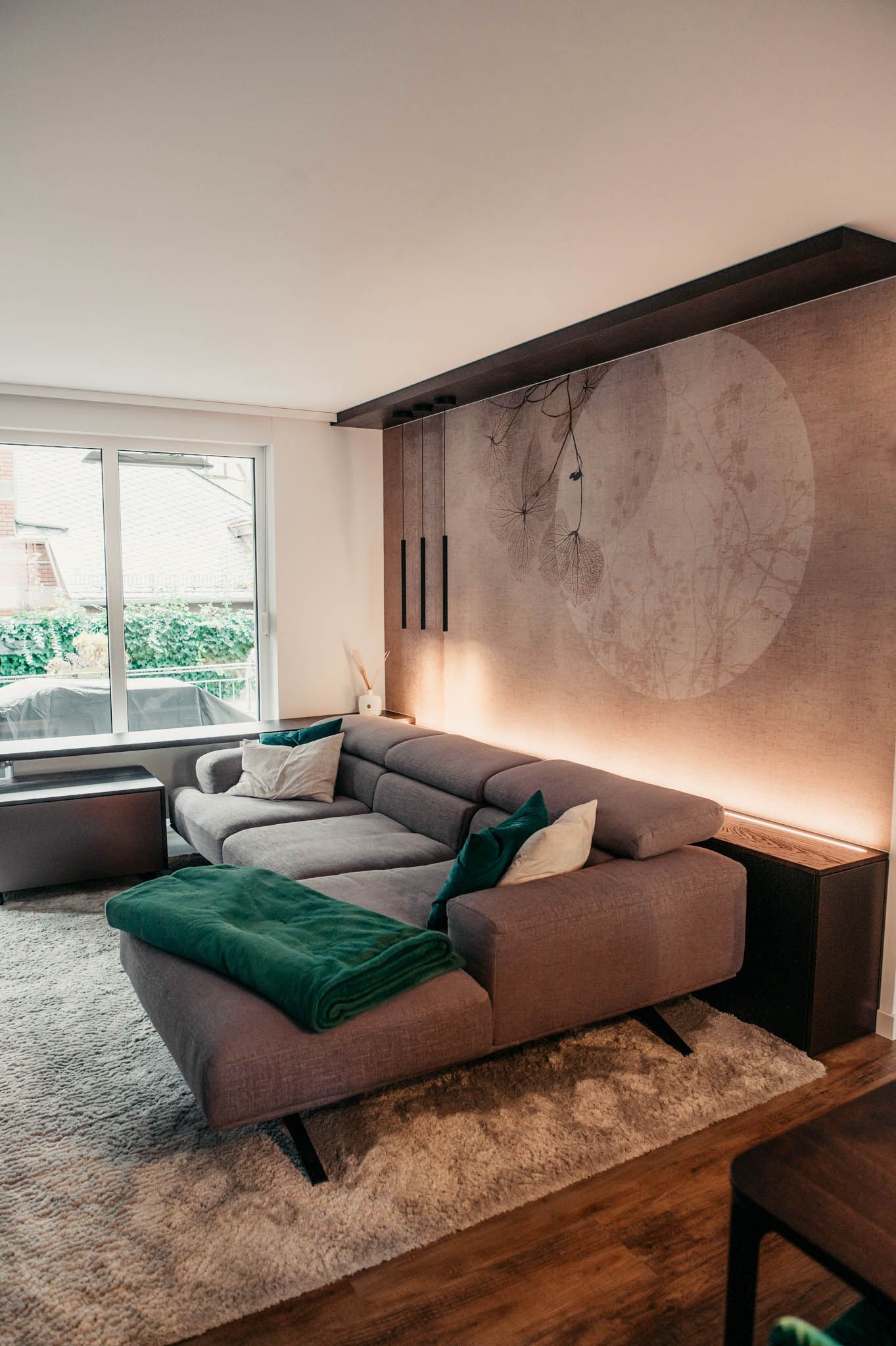 Wohnzimmer mit grauem Sofa, grüner Decke, strukturierter Wand mit kreisförmigem Design und Fenster.