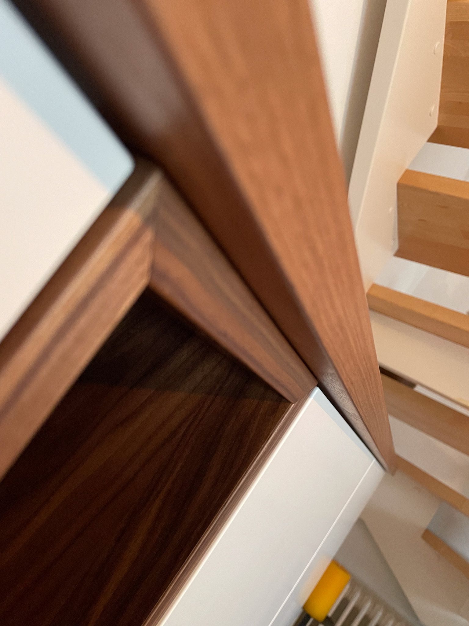 Nahaufnahme von Regalen mit Holzrahmen vor einer weißen Wand, aus einem Winkel betrachtet, mit einer Treppe im Hintergrund.