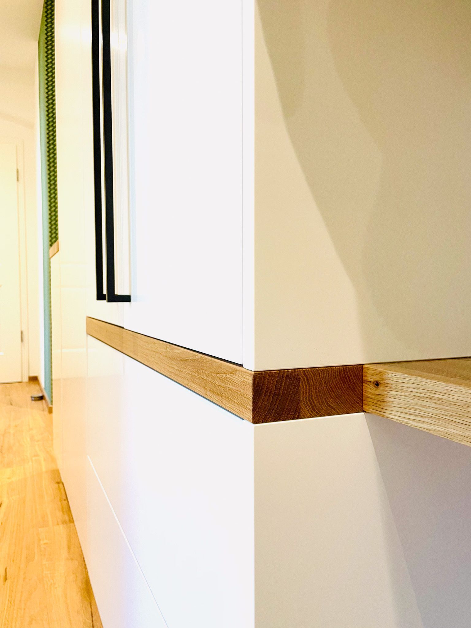 Weißer Schrank mit einem Holzregal an einer Wand. Nahaufnahme zeigt Regalkante und -ecke.