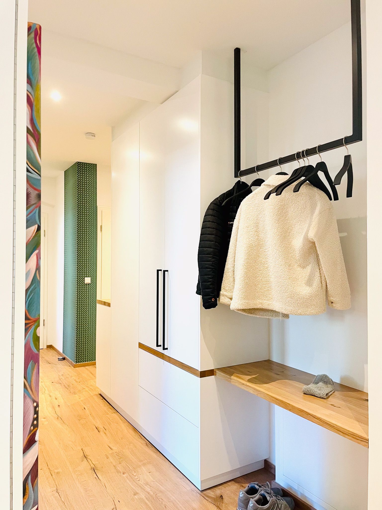 Flur mit weißem Schrank, Garderobe mit Jacken, Holzboden.