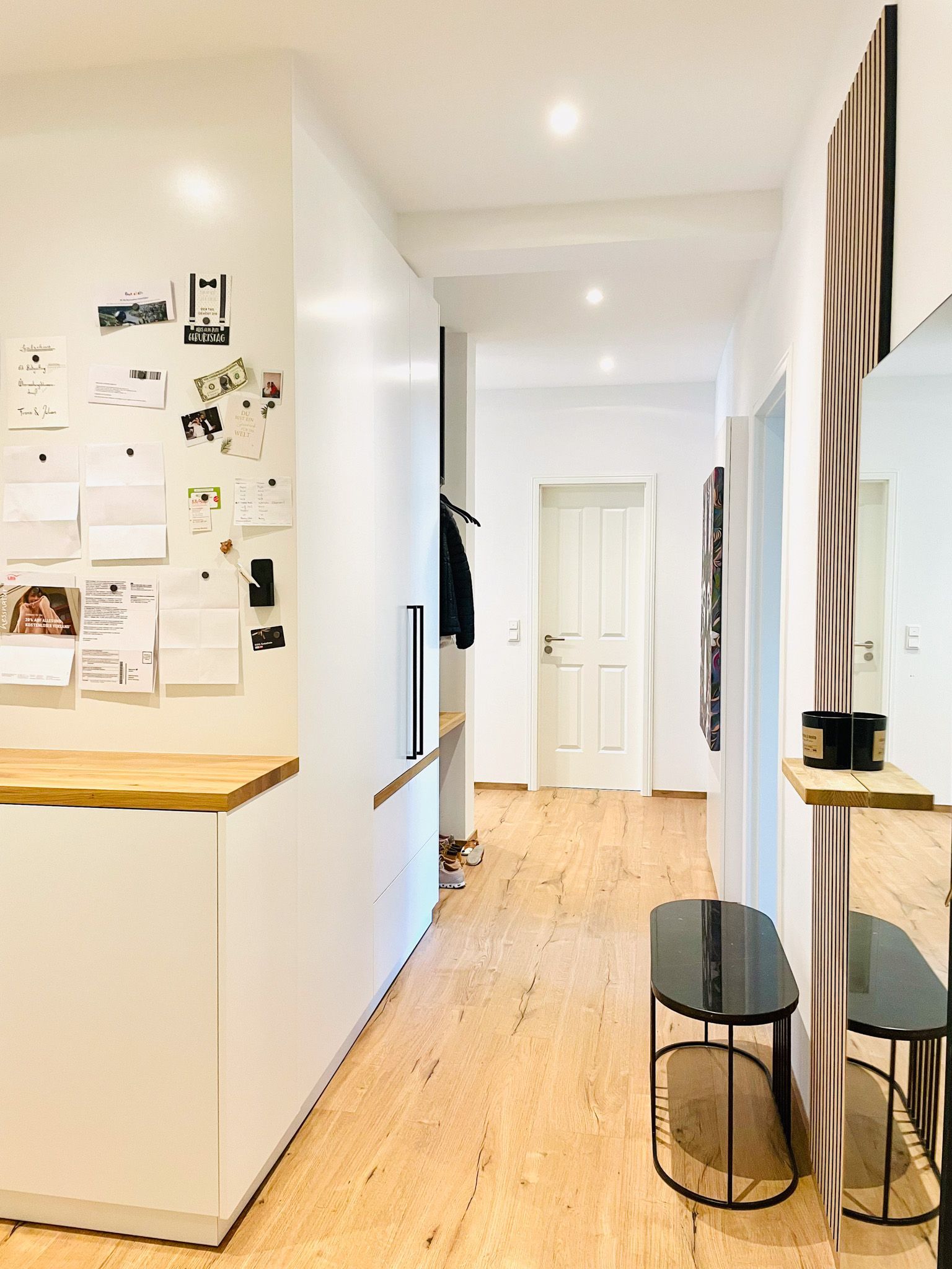 Schmaler Flur mit weißen Wänden, Holzboden und Bank. Am Ende befinden sich ein Spiegel, eine Garderobe und eine Tür.