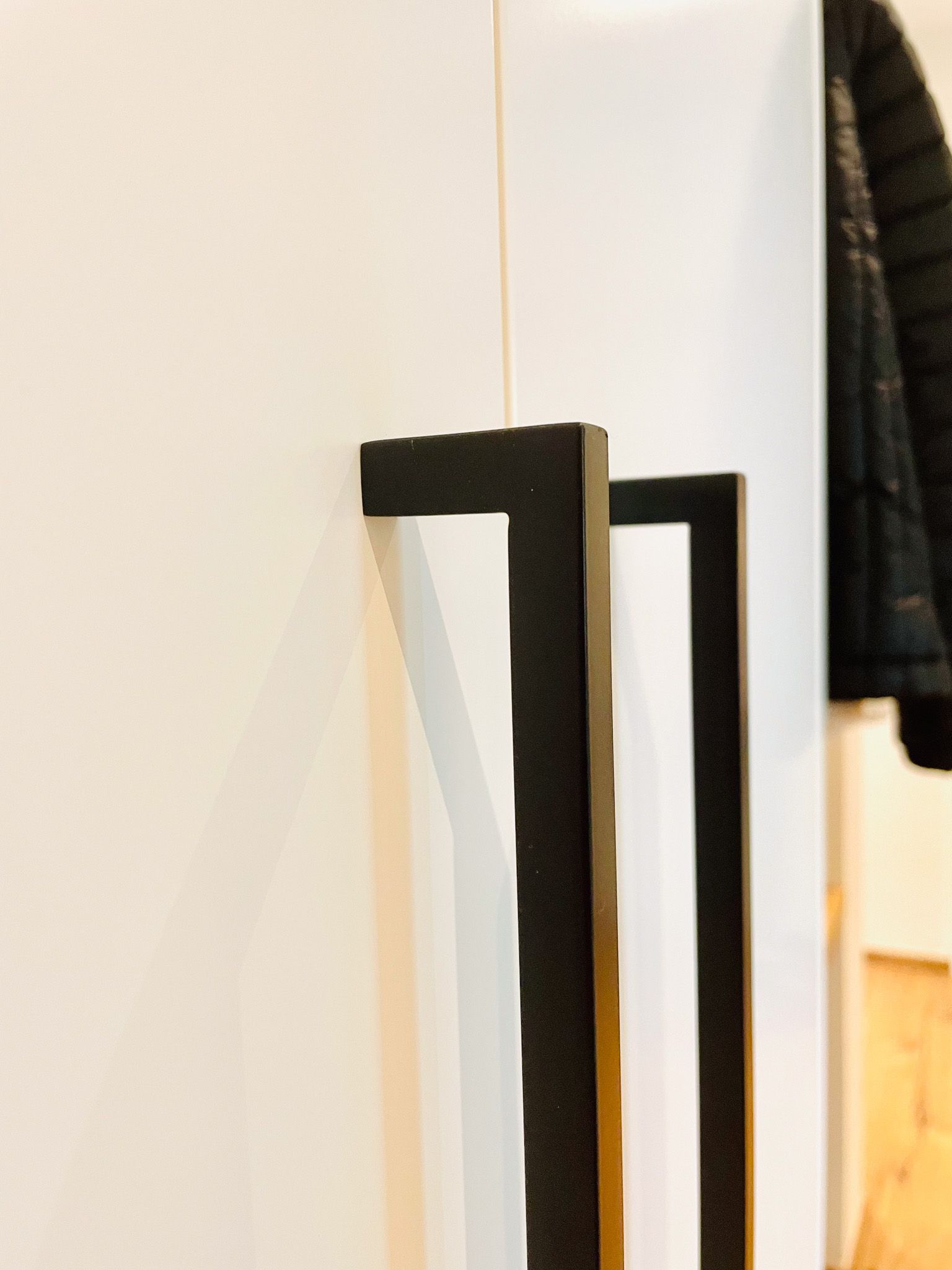 Zwei schwarze rechteckige Griffe an einer weißen Schranktür, Nahaufnahme.