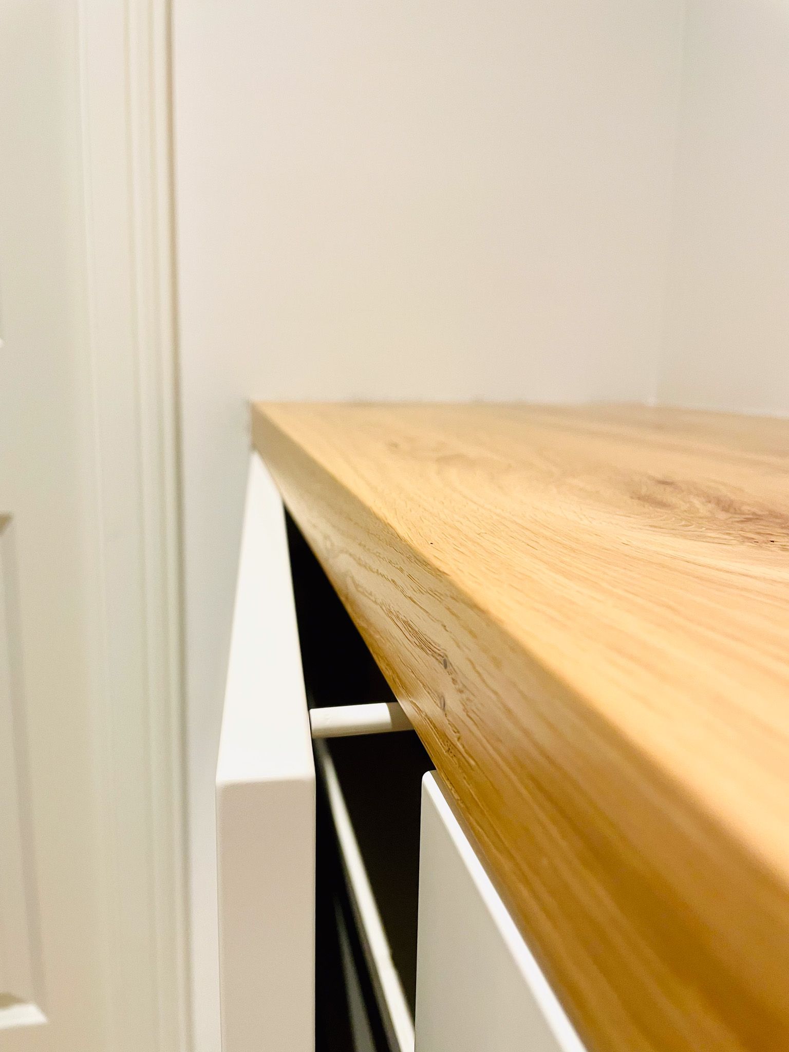 Nahaufnahme einer Arbeitsplattenkante aus hellem Holz über einem weißen Schrank vor einer weißen Wand.
