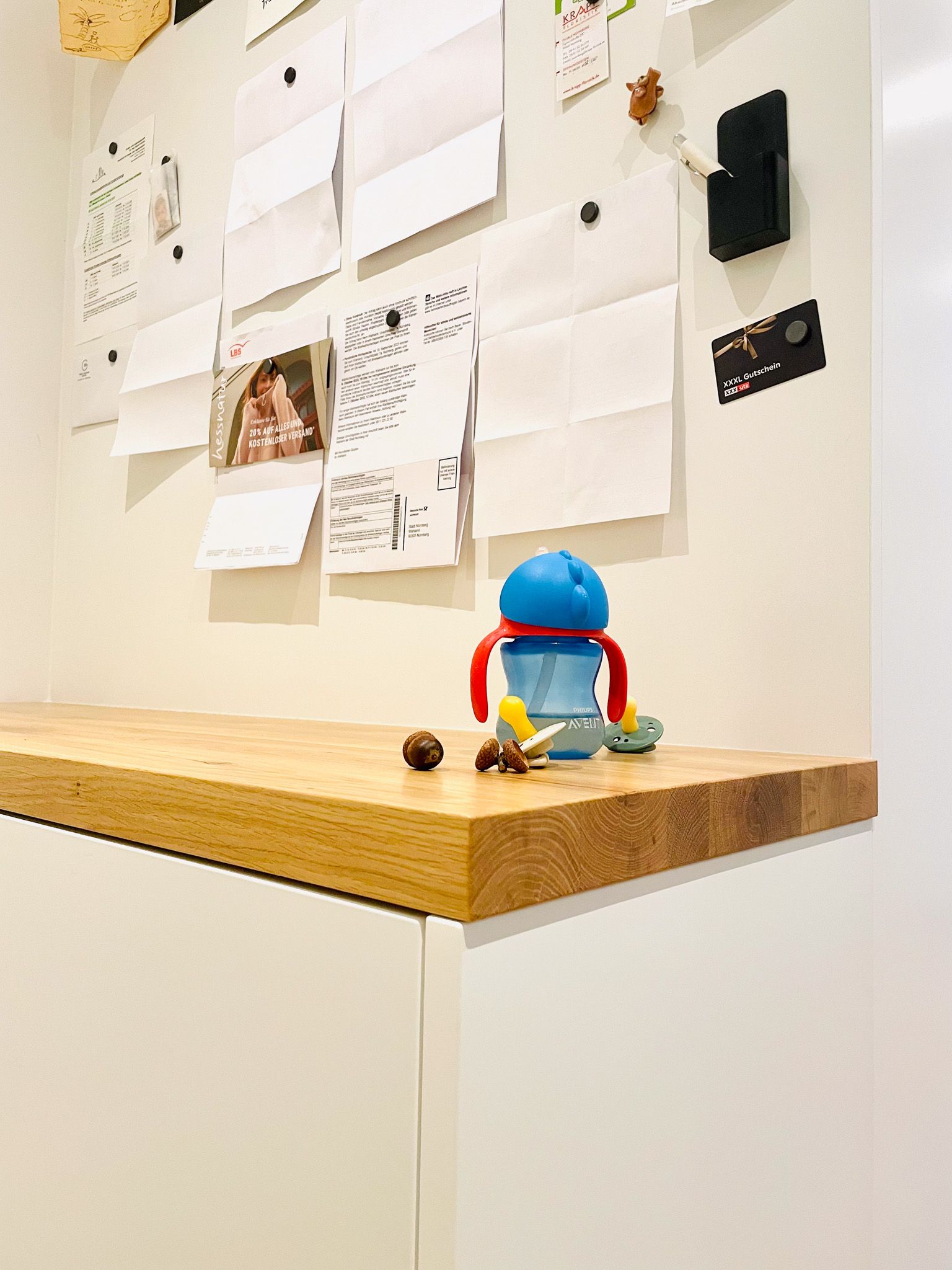 Holztheke mit blauem Trinkbecher, Snacks und einem weißen Schrank darunter. Im Hintergrund befindet sich eine Magnettafel mit Notizen.