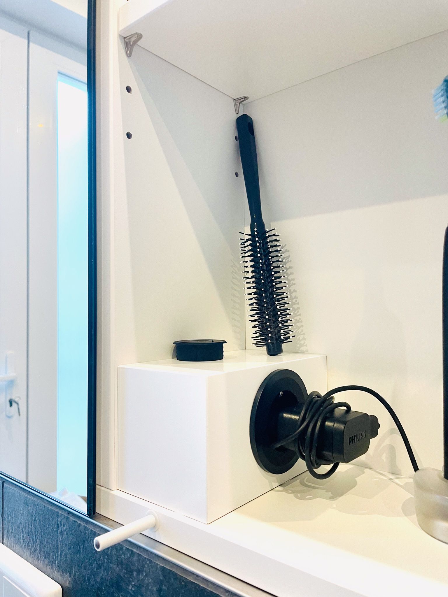 Weißer Badezimmerschrank mit Haarbürste, Lockenstab und Zubehör.