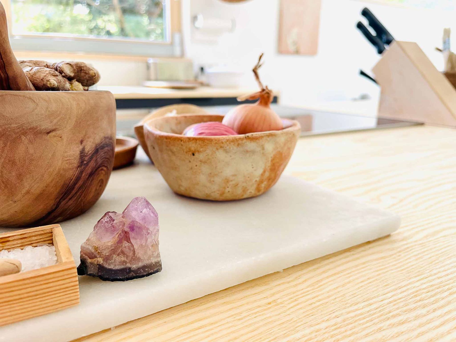 Holzschüsseln mit Zwiebeln, Gewürzen und einem Amethystkristall auf einer Küchentheke.