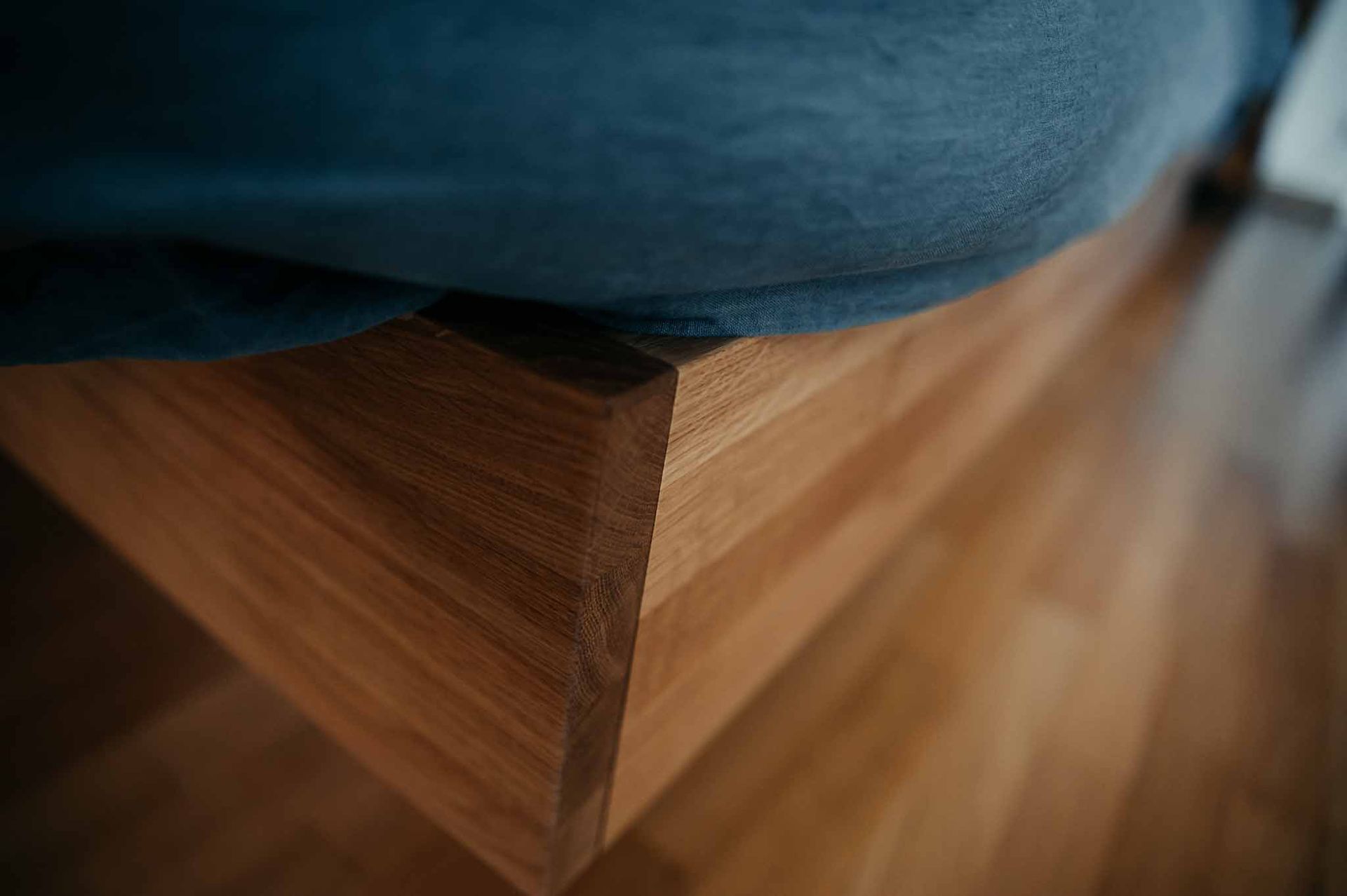 Person sitzt auf einer niedrigen Holzbank. Hellbraunes Holz, Blue Jeans, Inneneinrichtung.