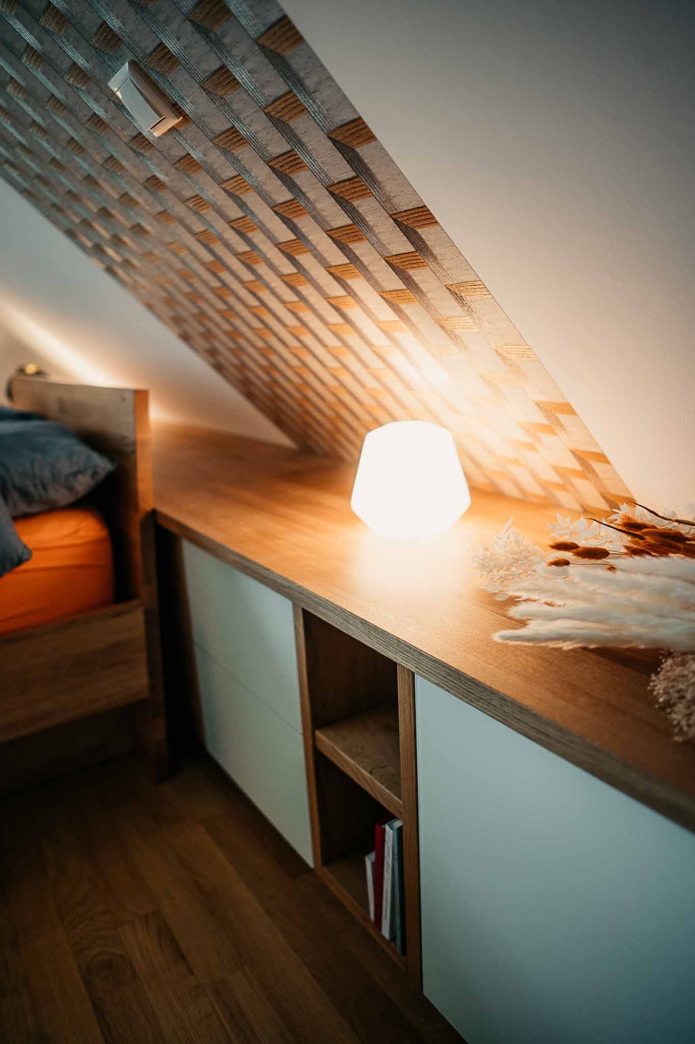 Gemütliches Dachgeschossschlafzimmer mit eingebautem Holzregal, leuchtender Lampe und Büchern.
