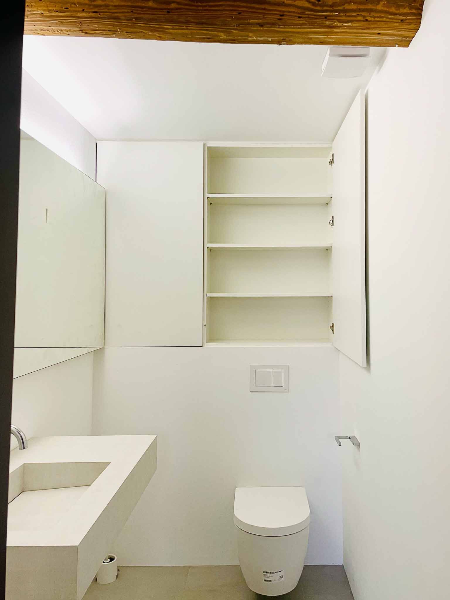 Ein kleines, weißes, minimalistisches Badezimmer mit Toilette, Waschbecken und offenem Schrank.