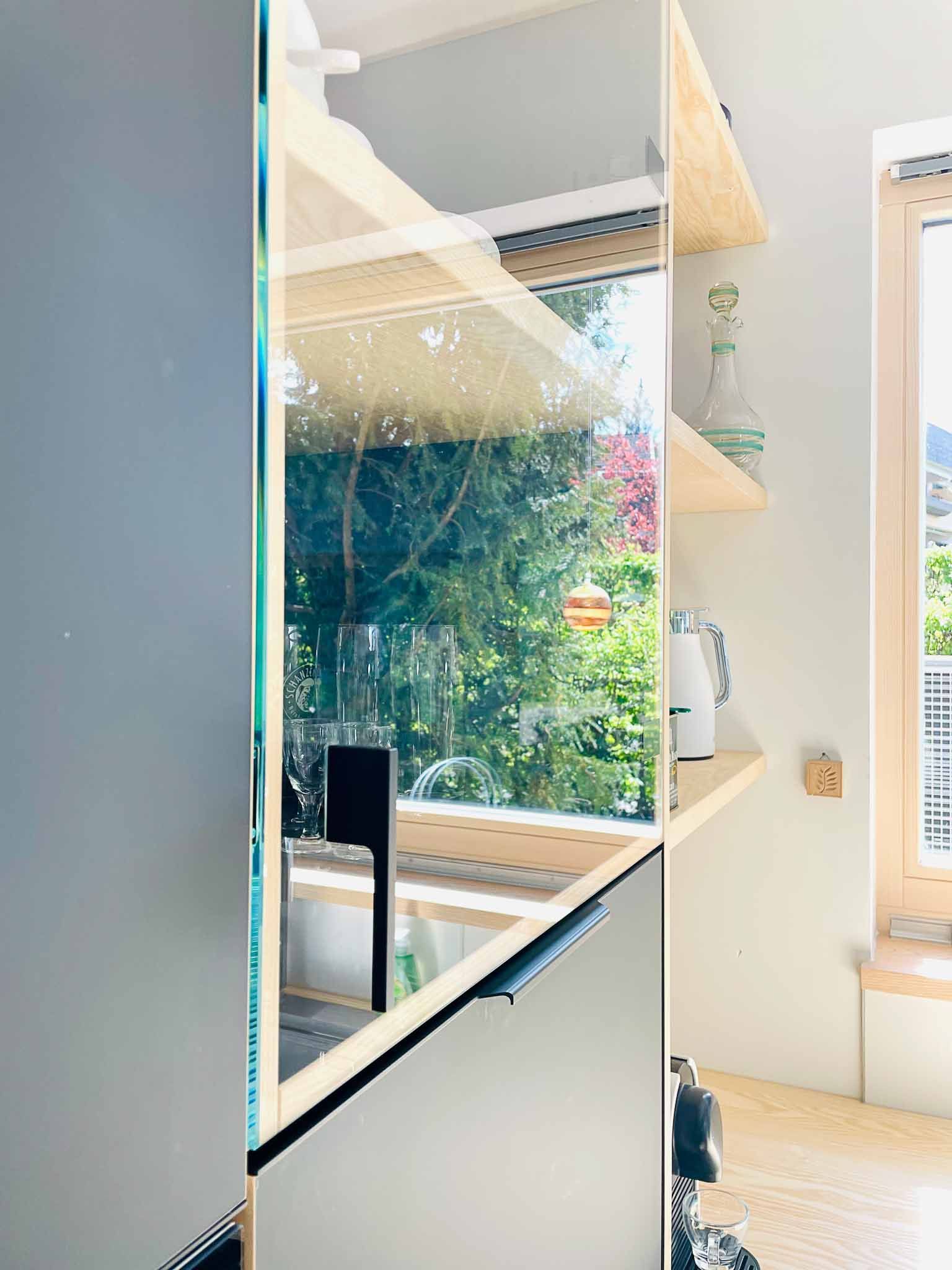 Moderne Speisekammerküche mit Glasregalen, die teilweise Grün reflektieren.