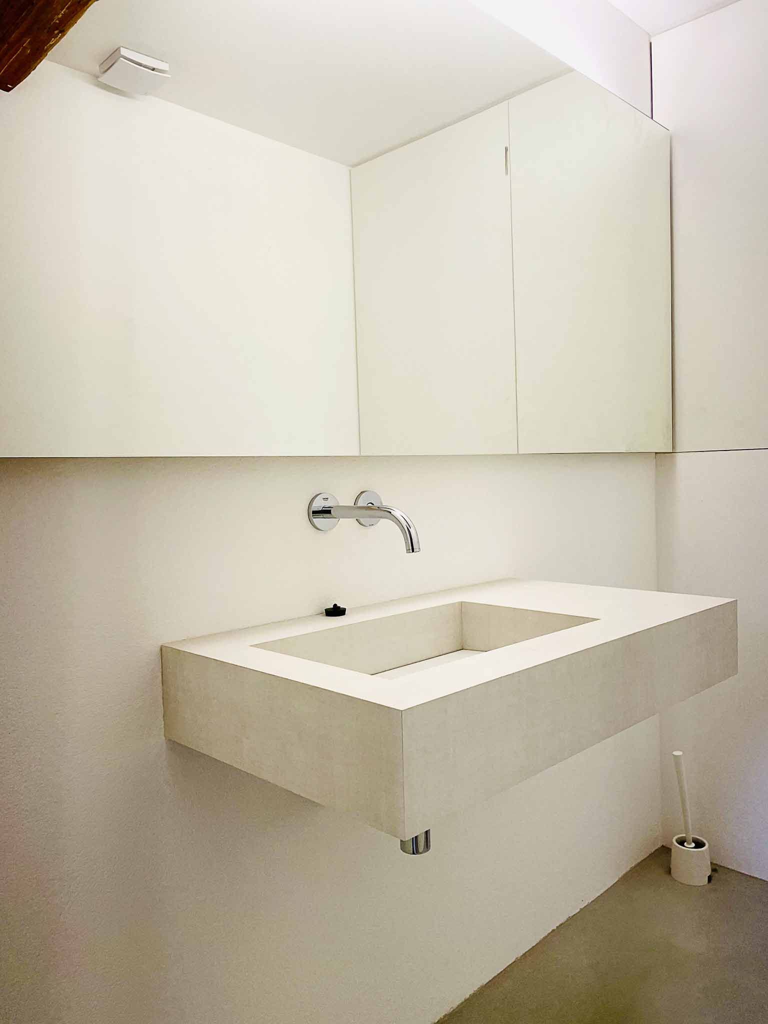 Modernes weißes schwebendes Waschbecken in einem minimalistischen Badezimmer mit großem Spiegel und Toilettenbürste.