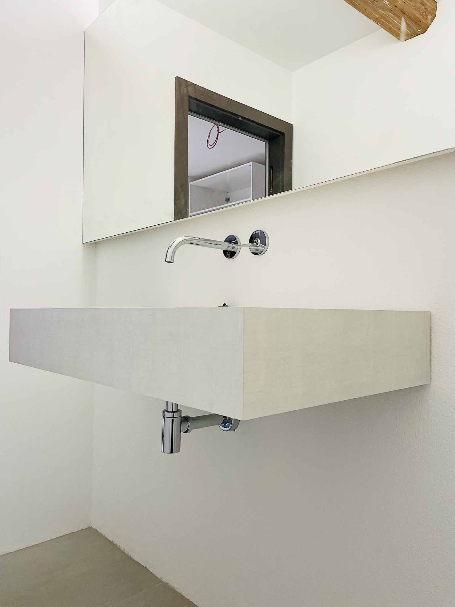 Modernes Badezimmer mit einem weißen, schwebenden Waschbecken und einem Chromhahn, an einer weißen Wand montiert.