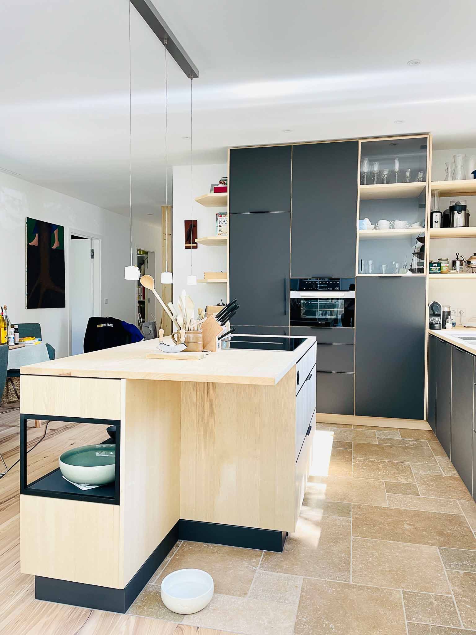 Moderne Küche mit heller Holzinsel, grauen Schränken und Steinböden.