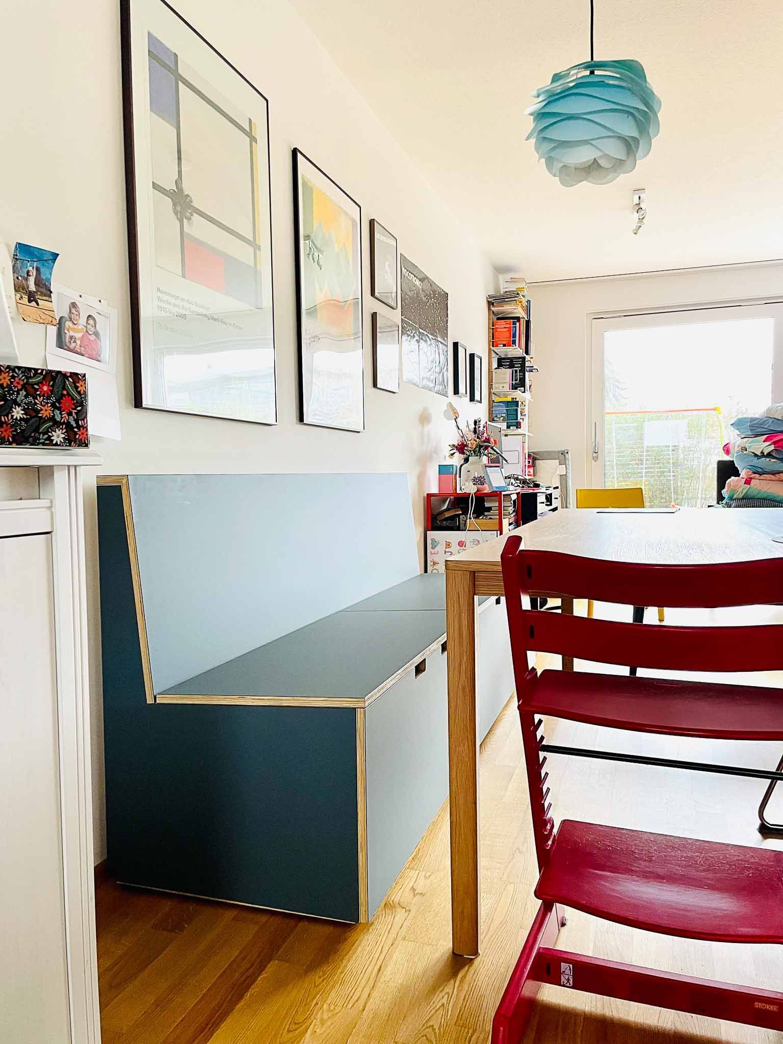 Ein Essbereich mit einer eingebauten blauen Bank, Kunstwerken und einem roten Stuhl.