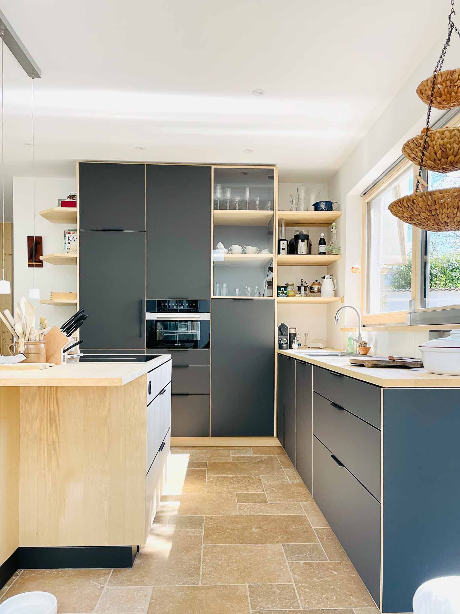 Moderne Küche mit grauen Schränken, Holzinsel und beigem Steinboden.