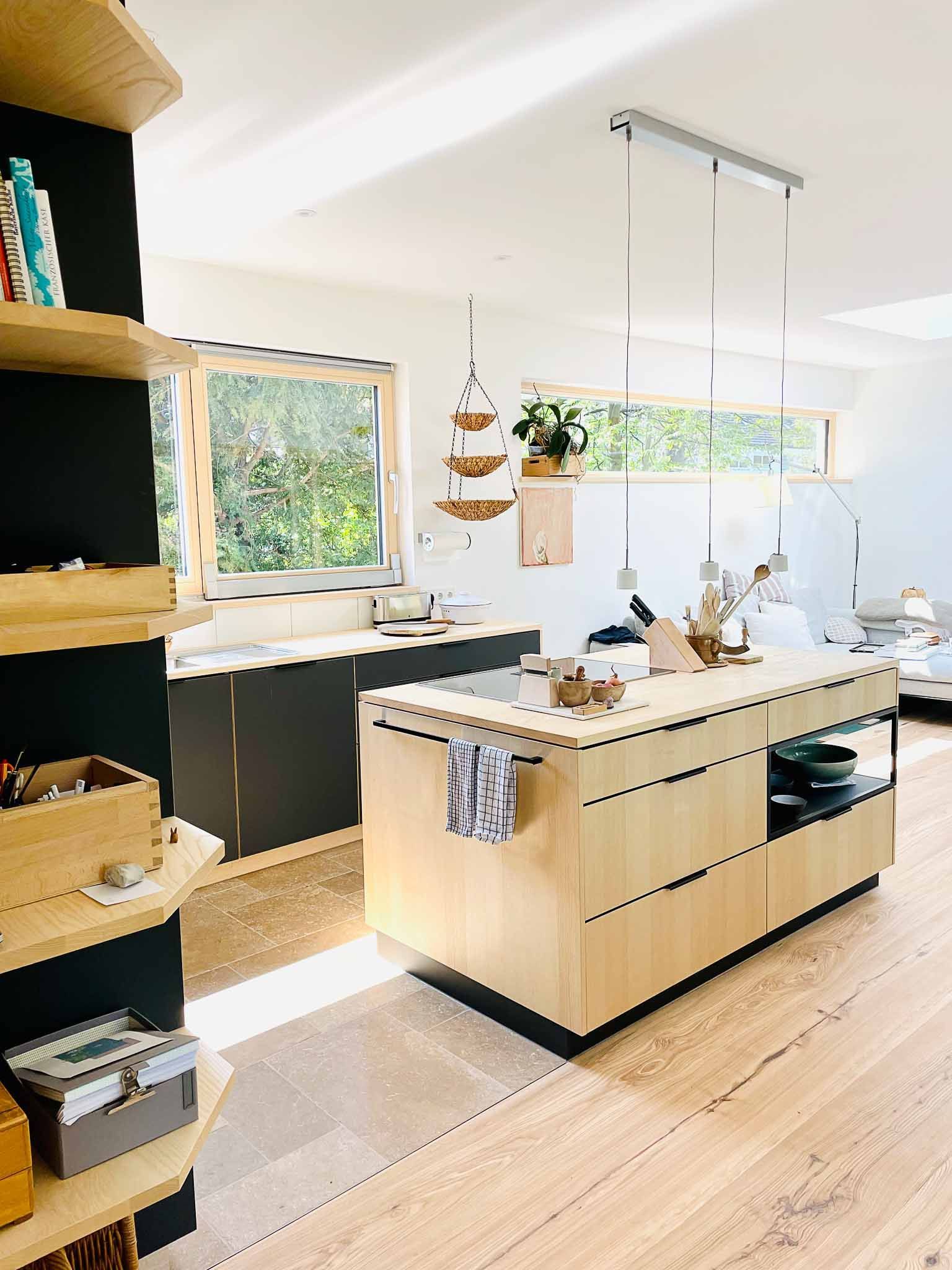 Moderne Küche mit heller Holzinsel, dunklen Schränken, offenen Regalen und großem Fenster.