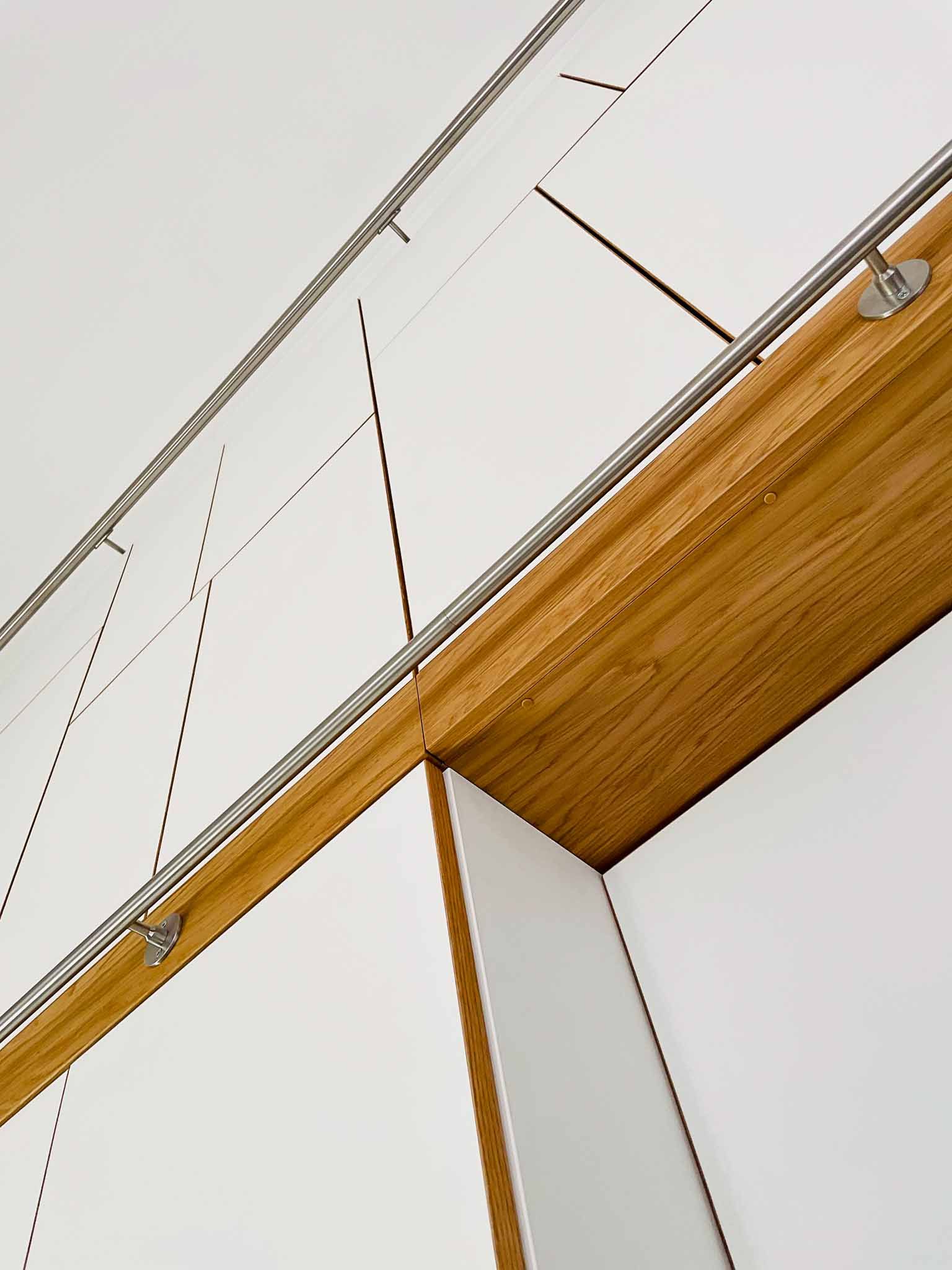 Weiße Wand mit Holzverkleidung, darüber gespannte Stahlkabel.