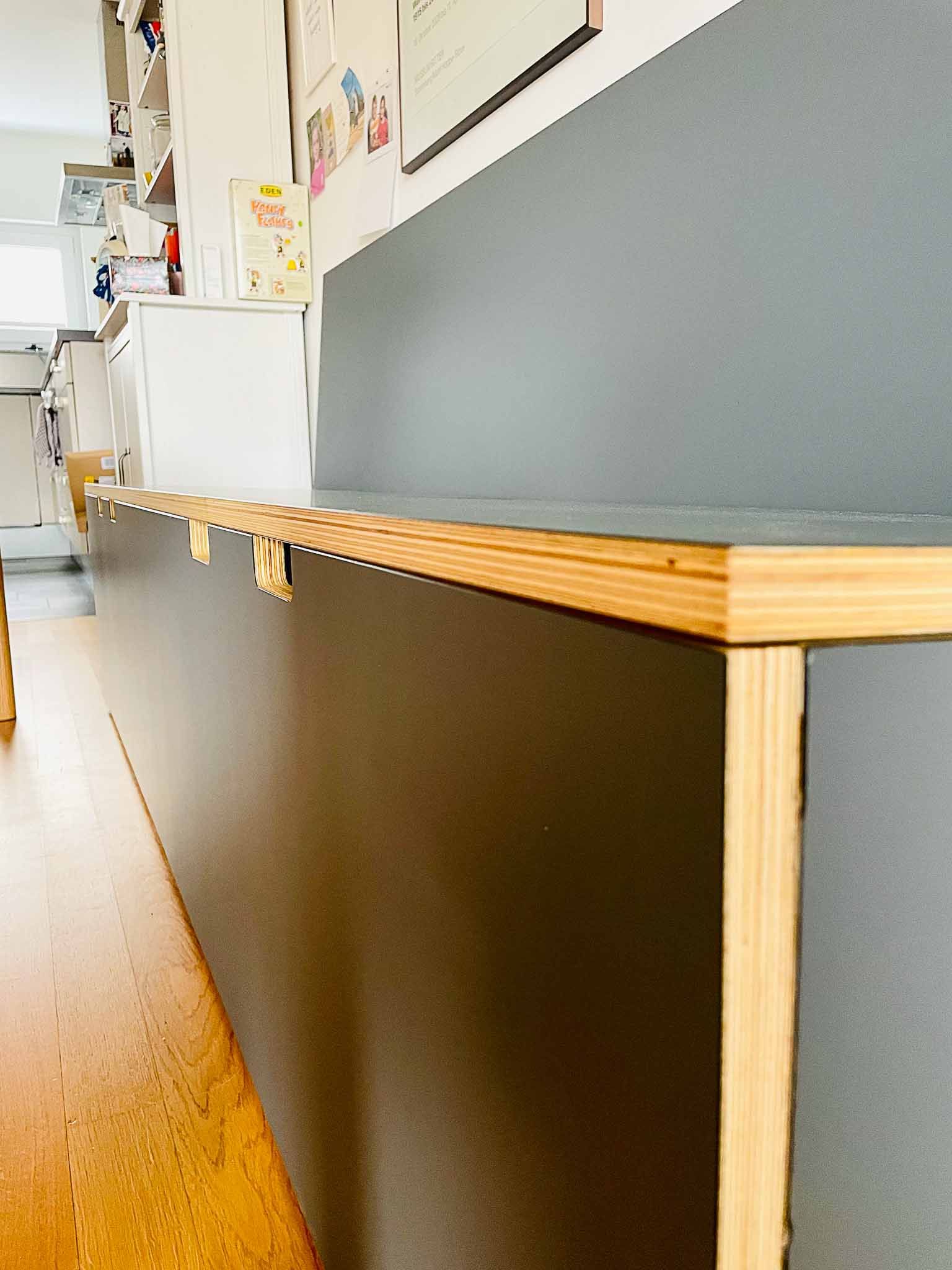 Dunkelgraue Einbaubank mit Holzkante in einem Raum mit hellem Holzboden.