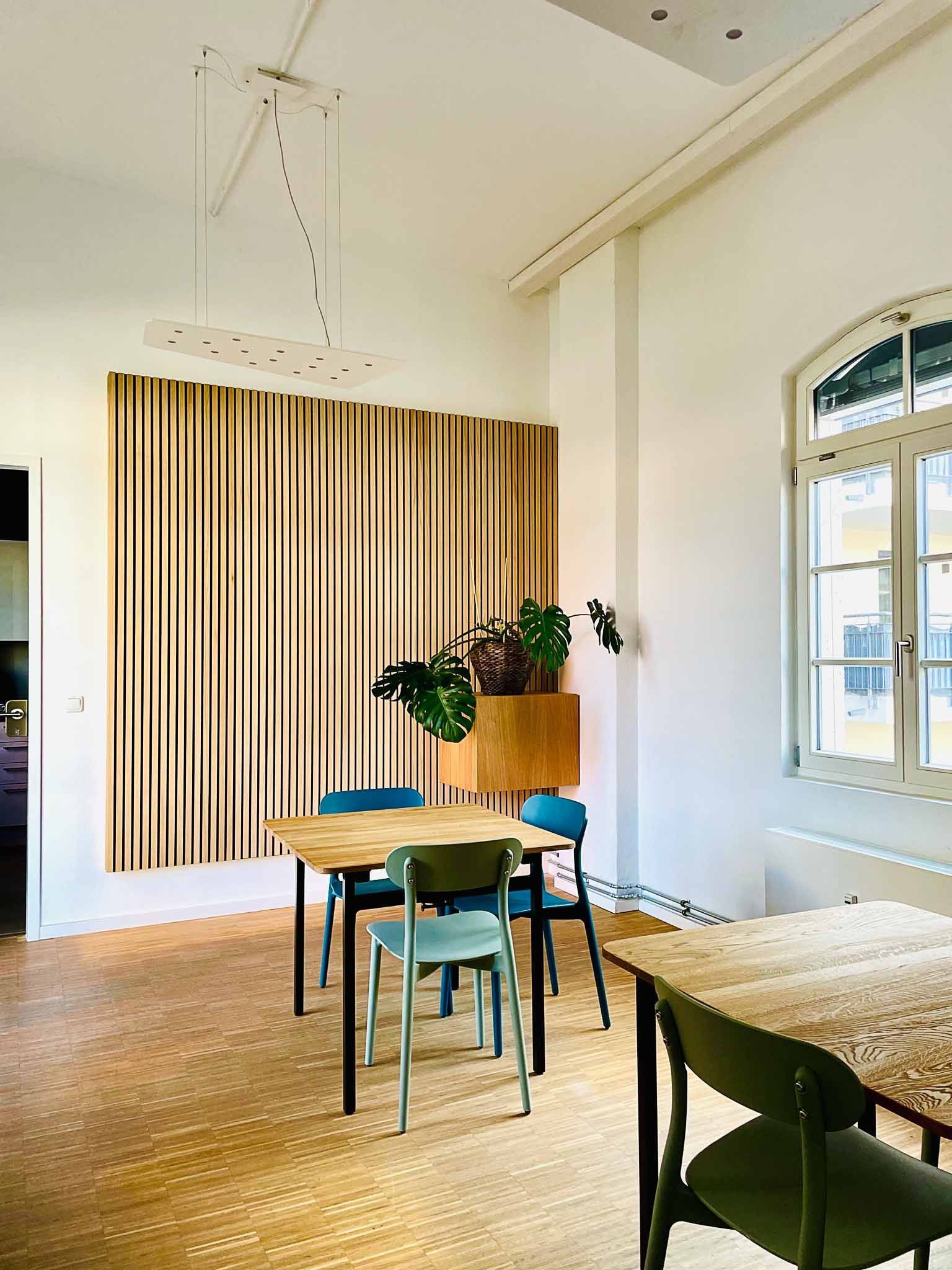 Essbereich mit Holztisch, Stühlen und vertikaler Holzvertäfelung an der Wand. Natürliches Licht durch das Fenster.