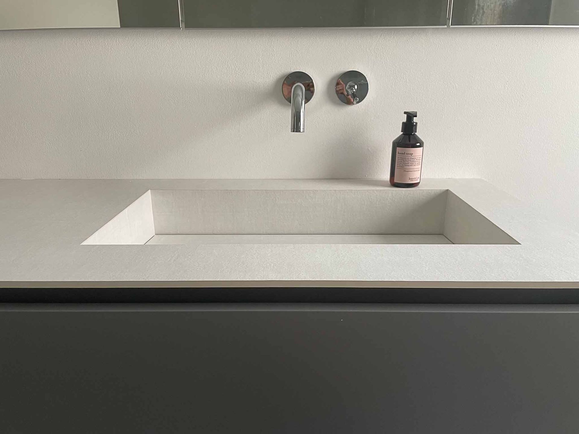 Weißes, modernes Badezimmerwaschbecken mit grauem Schrank, Chromhahn und Seifenspender.